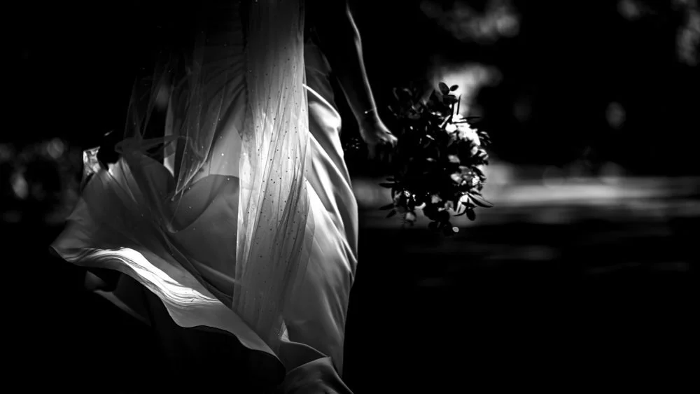 A person in a flowing dress holding a bouquet of flowers, captured in black and white.
