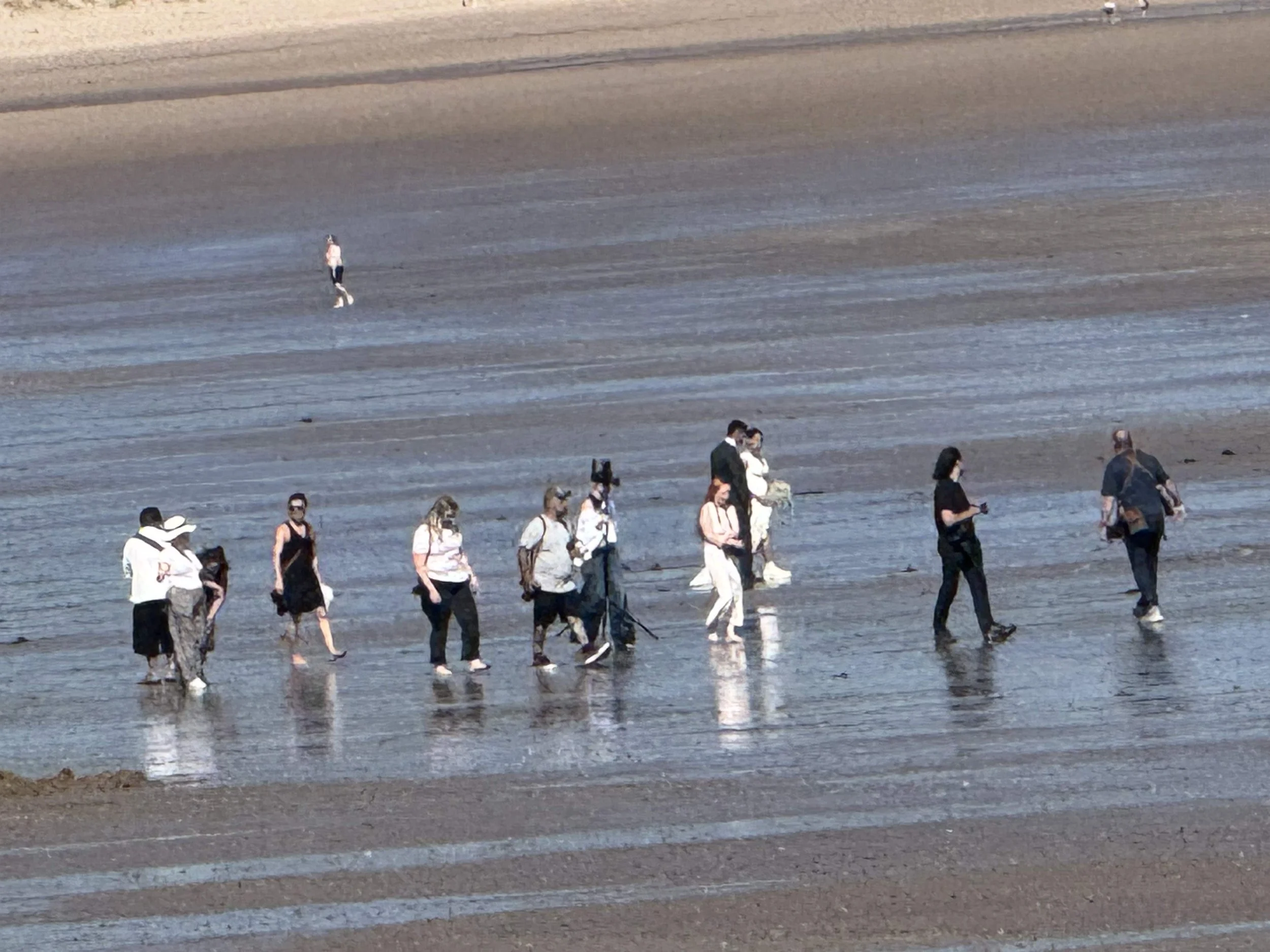 A group of people walking on a wet, sandy beach, some wearing masks and casual clothing.