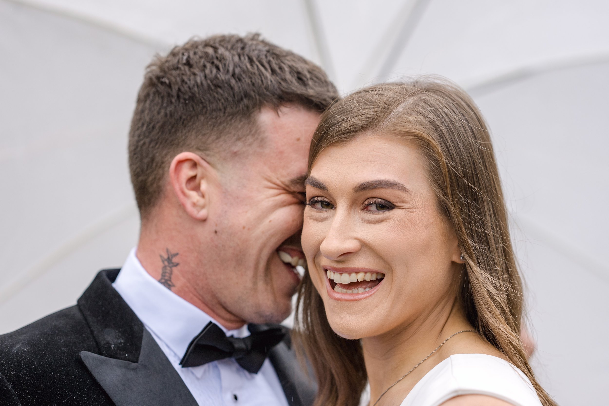 A happy couple smiling and laughing, dressed in formal wedding attire, close-up portrait.