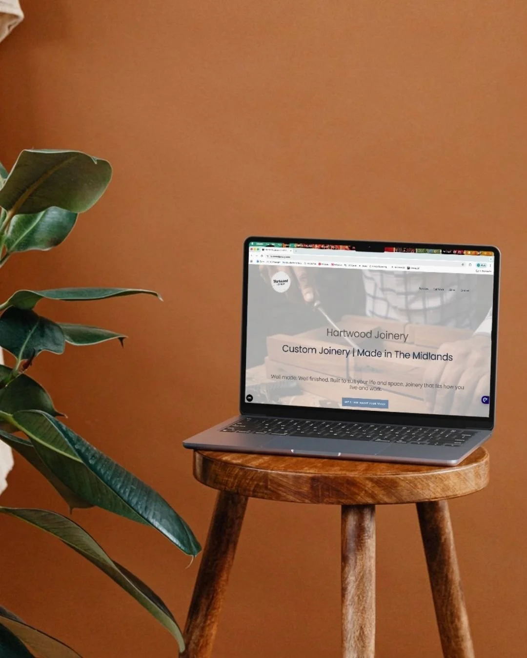 Laptop sits on wooden stool with the newly designed Hartwood Joinery home page displayed on screen
