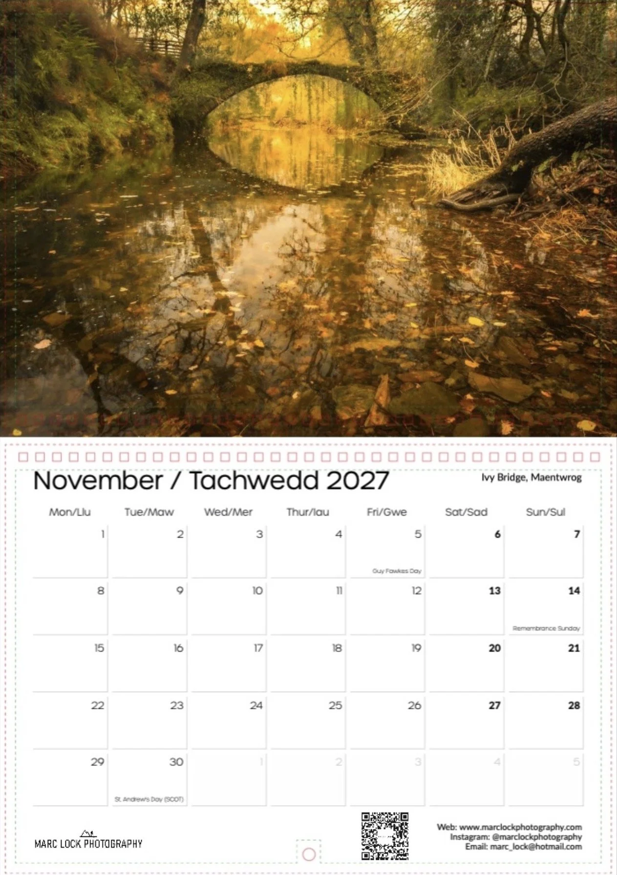 Autumn scene of a creek with a stone bridge reflecting in the water, surrounded by trees with fall foliage, at sunset.