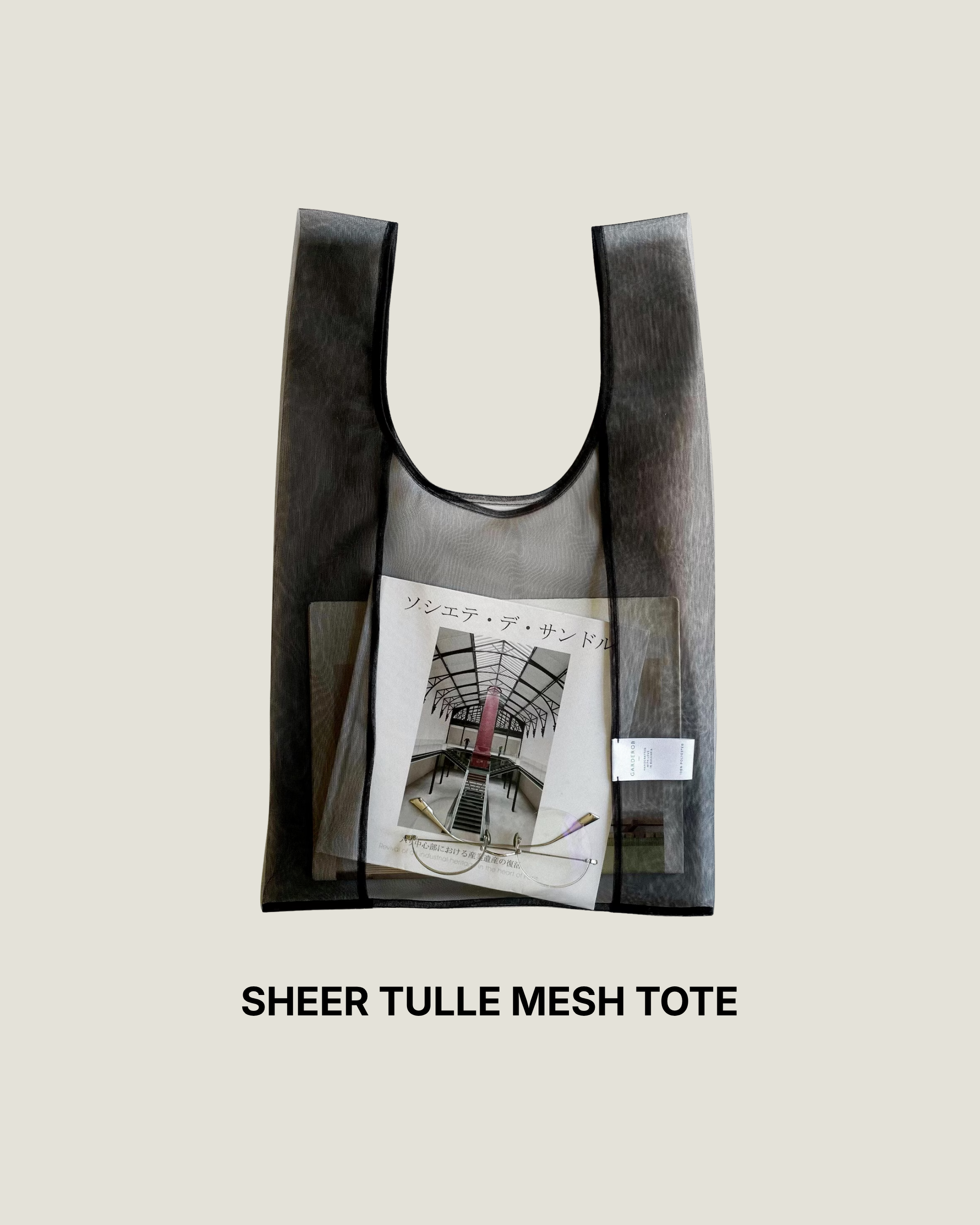 Sheer black tulle mesh tote bag holding a magazine, laid flat on a white background