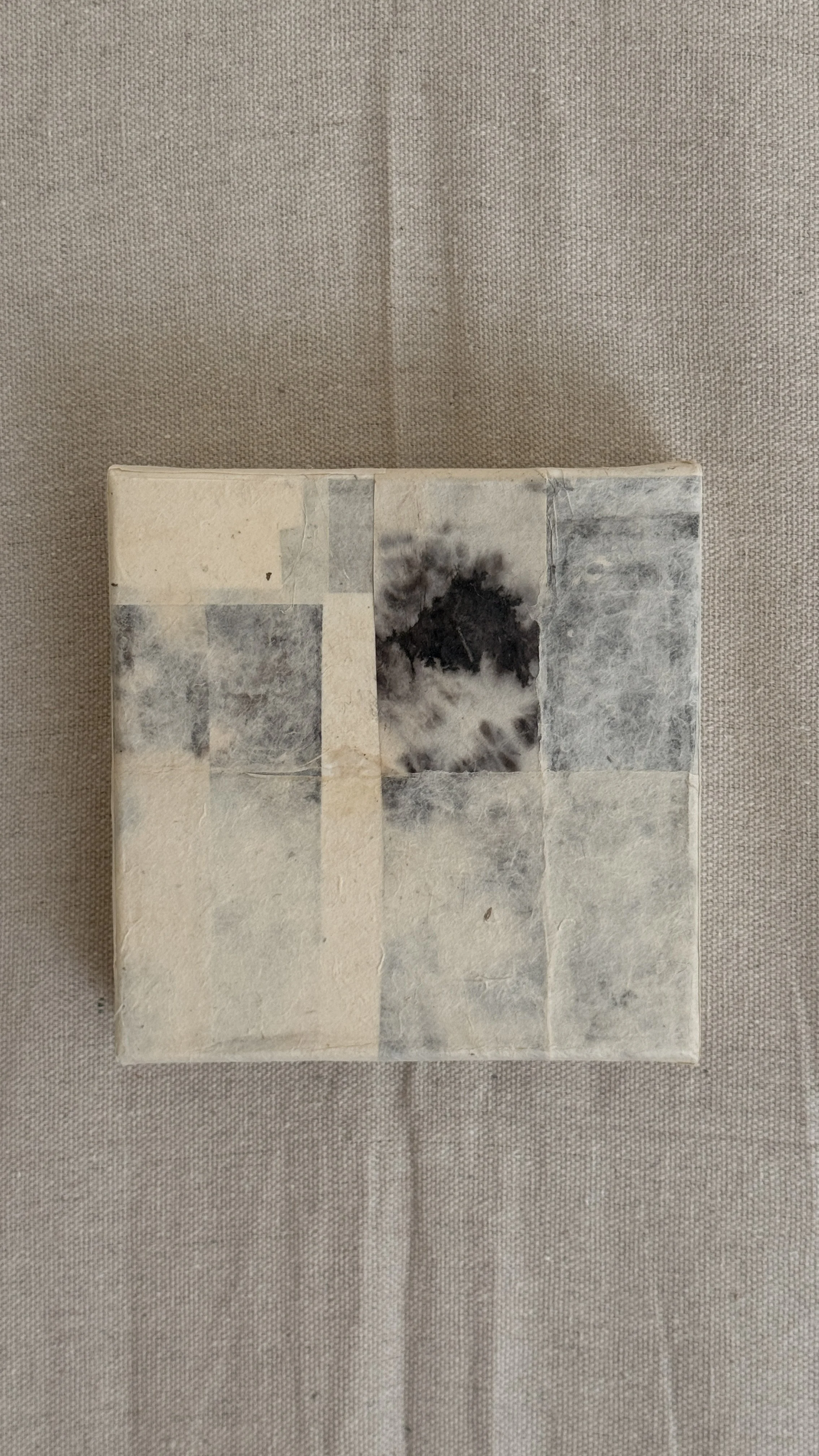 Small abstract collage of layered cream and grey handmade papers with a dark bloom-like mark near the top, unframed 6x6 art
