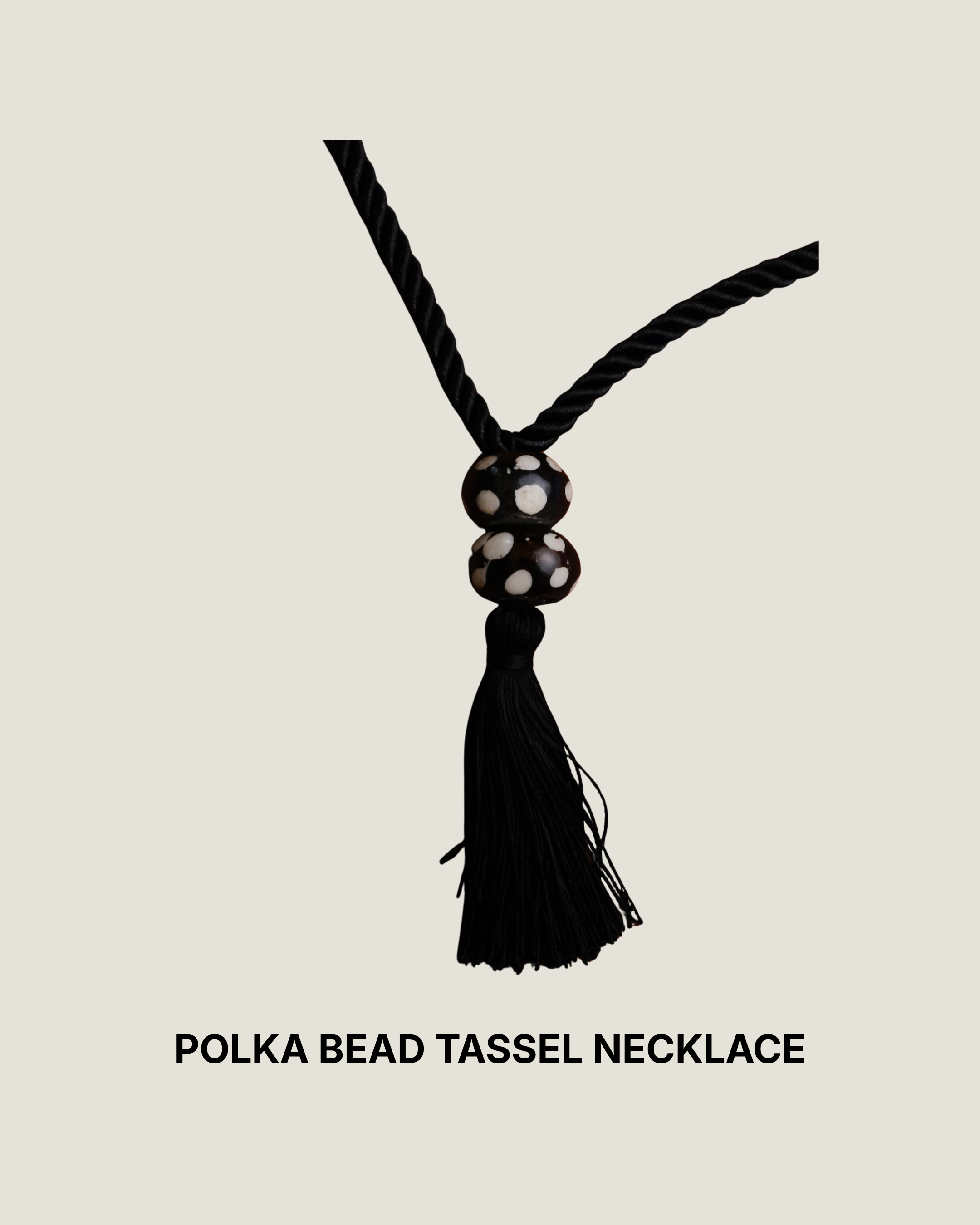 Polka dot batik wood bead tassel necklace on black silk rope against rust-brown fabric