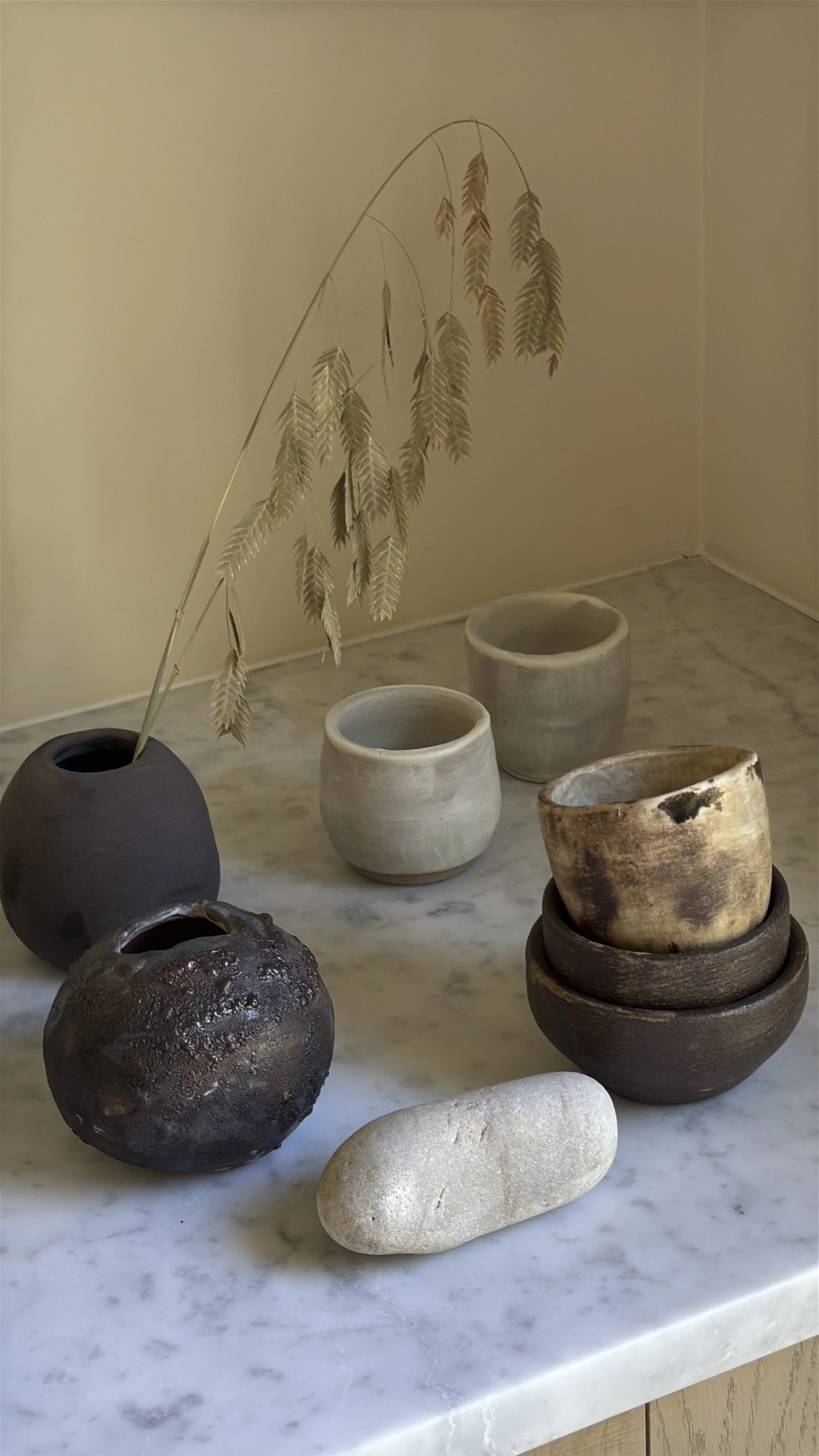 Tapered ceramic cup in warm caramel and sand tones with dark smoky patches on the surface and a pale interior