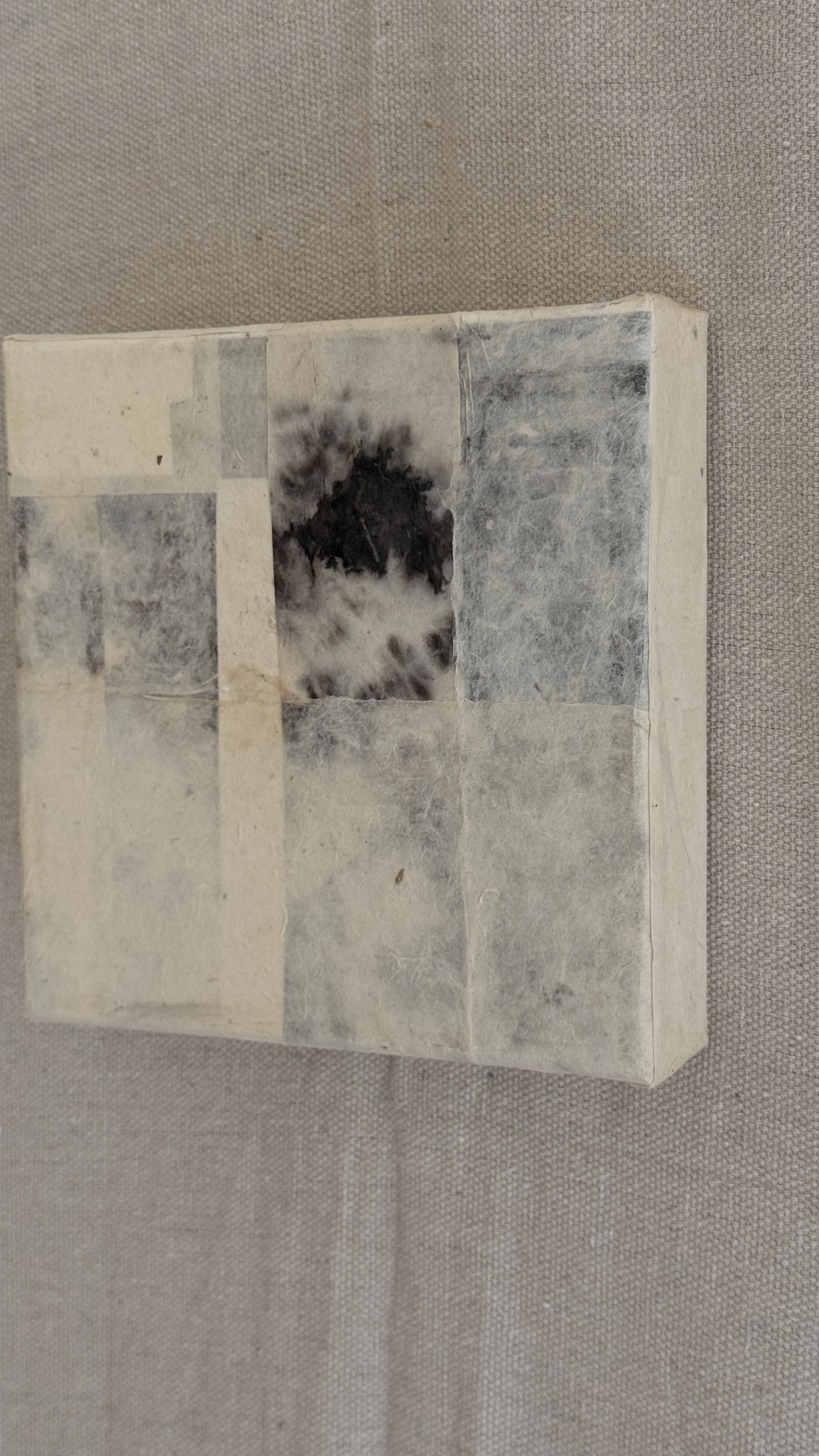 Small abstract collage of layered cream and grey handmade papers with a dark bloom-like mark near the top, unframed 6x6 art