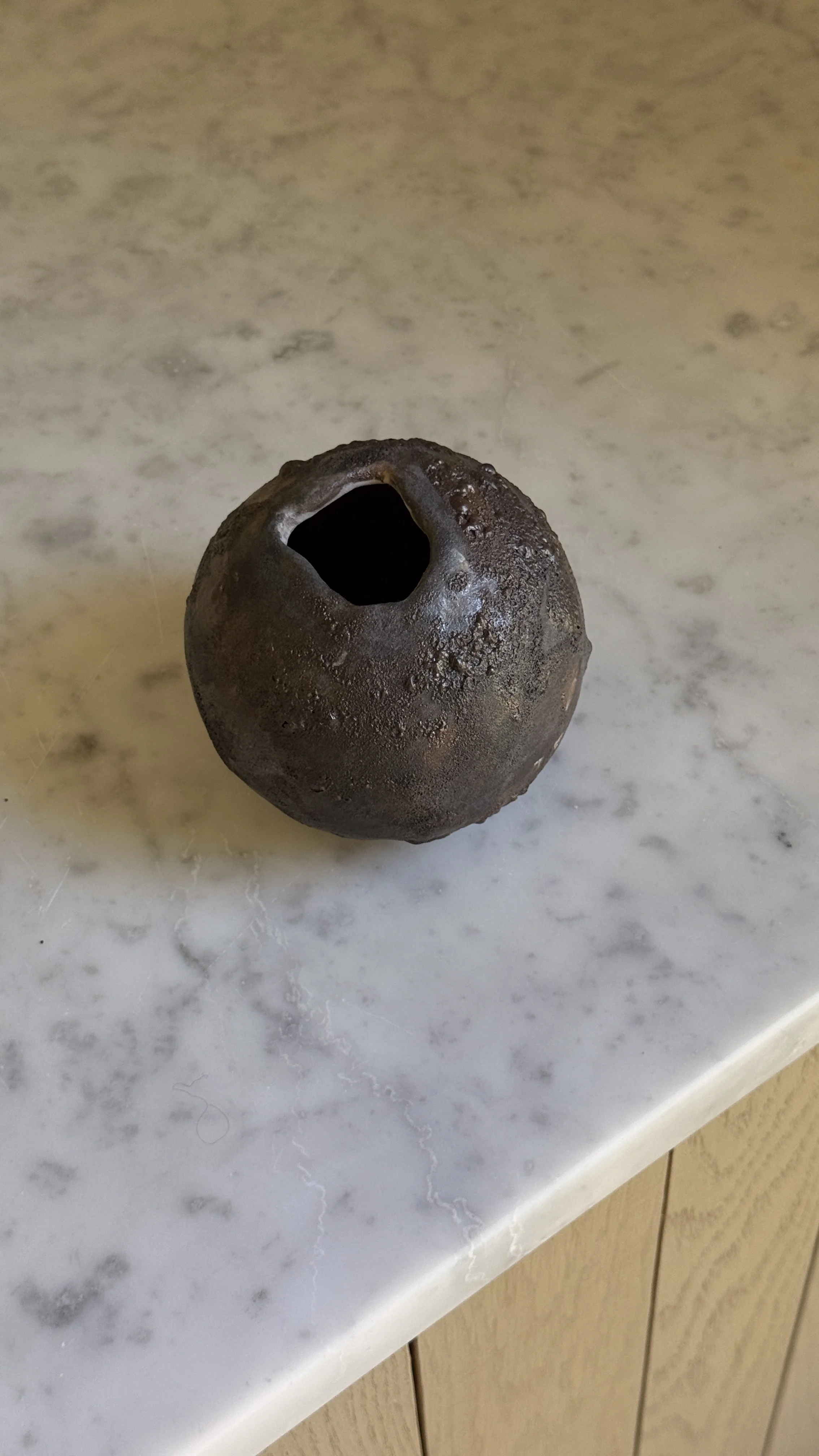 Round dark ceramic moon vase with a textured lava glaze in brown, charcoal, and bronze, and a small opening at the top