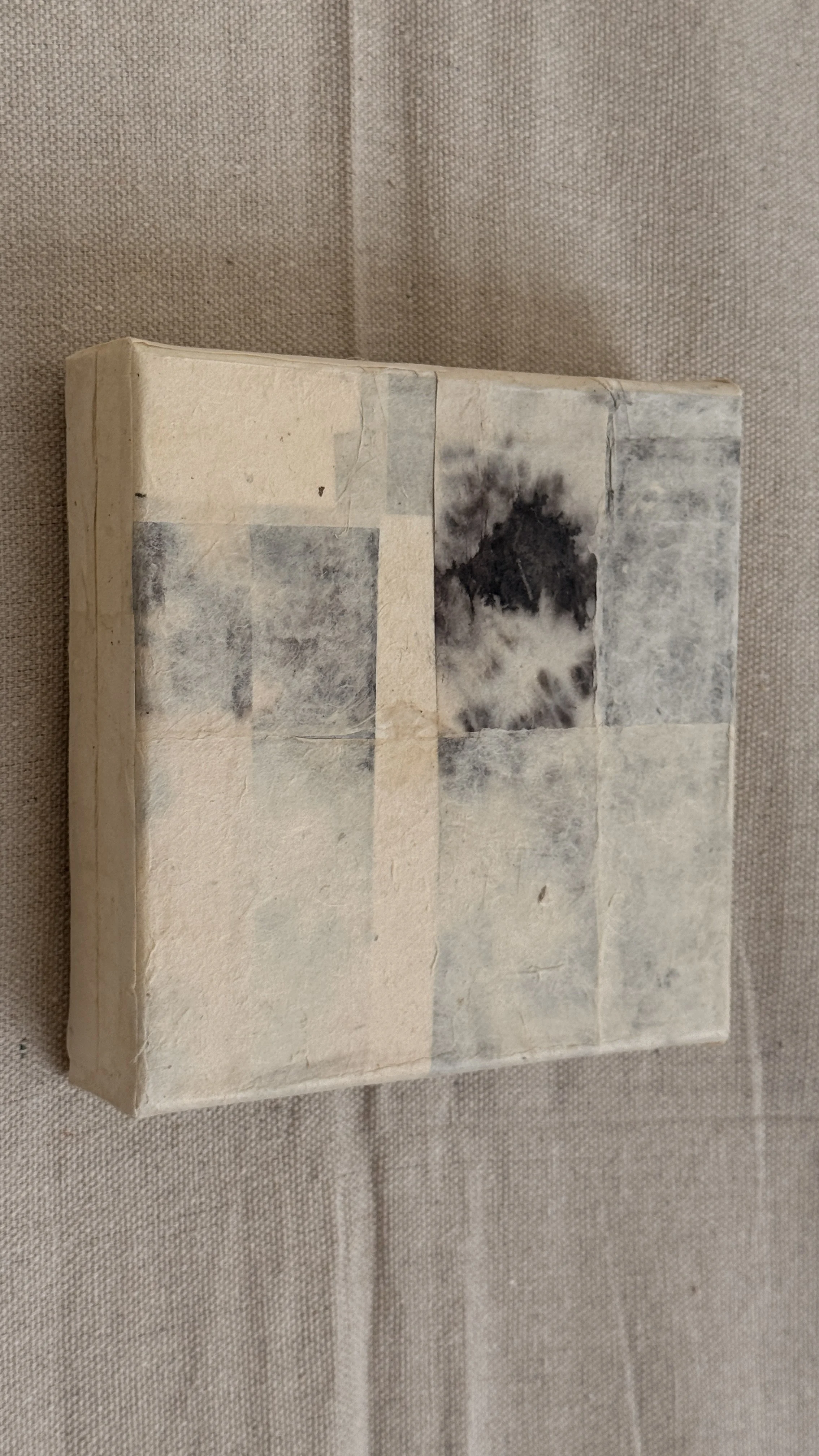 Small abstract collage of layered cream and grey handmade papers with a dark bloom-like mark near the top, unframed 6x6 art