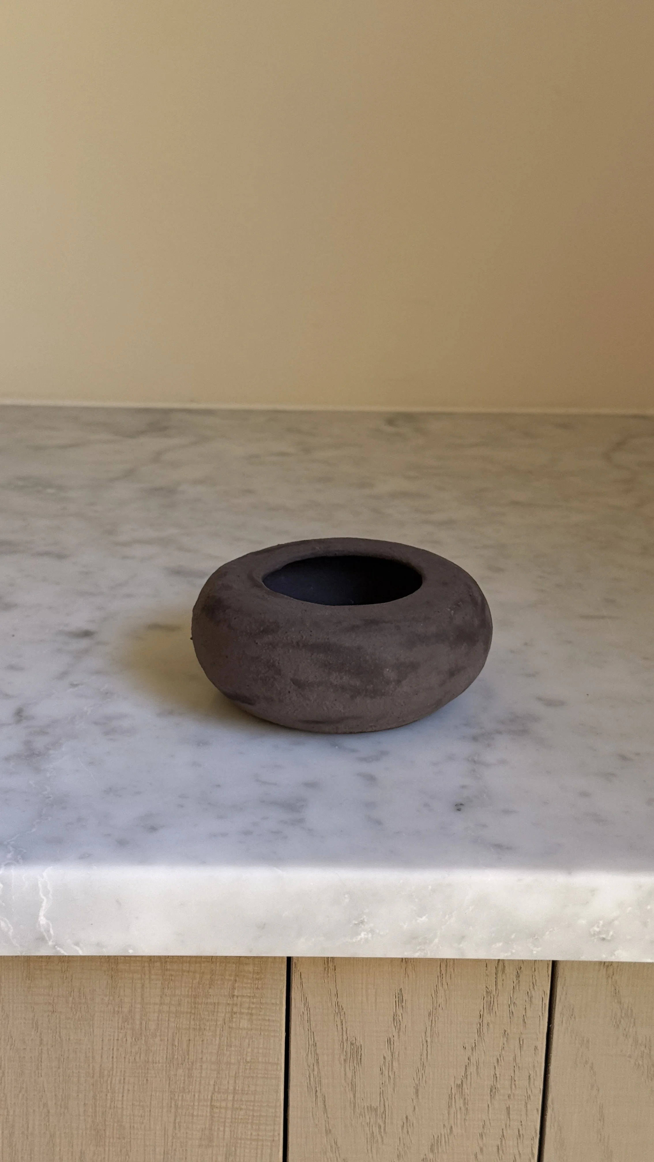 Low rounded dark brown matte ceramic vessel shaped like a river stone with a small opening and black interior