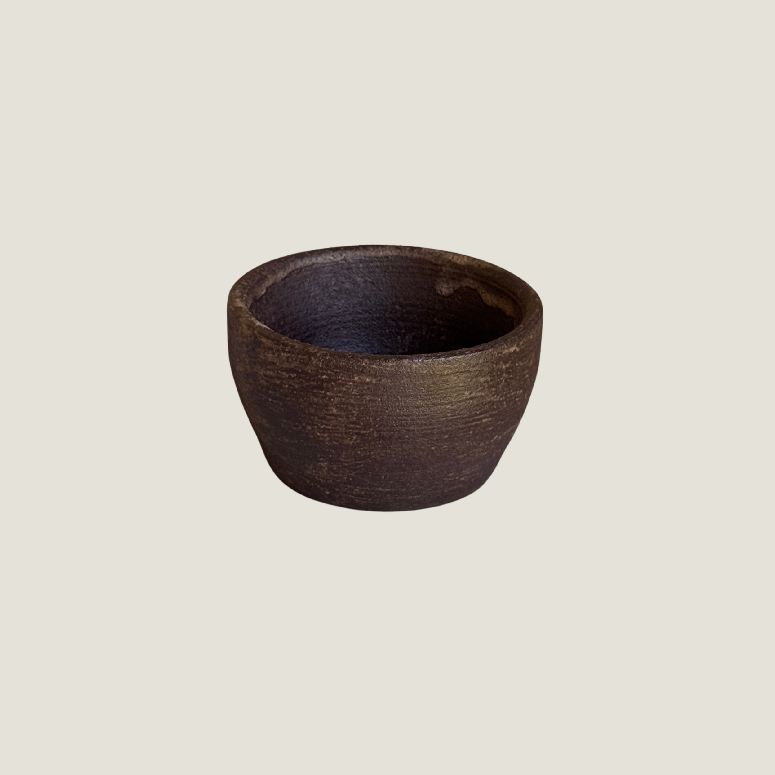 Dark brown ceramic bowl with horizontal brushed texture and warm bronze highlights, tapered base, greige background