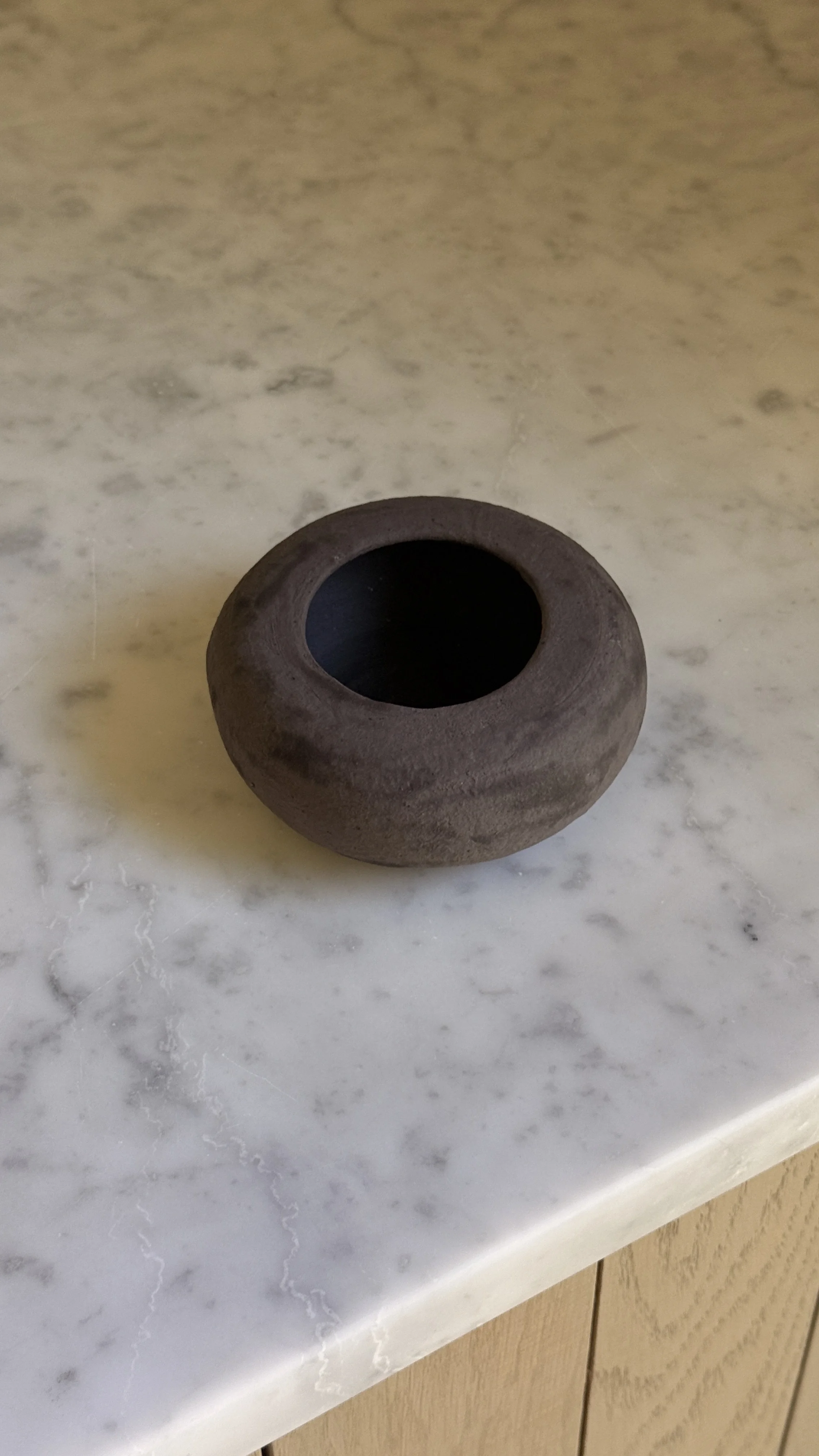 Low rounded dark brown matte ceramic vessel shaped like a river stone with a small opening and black interior