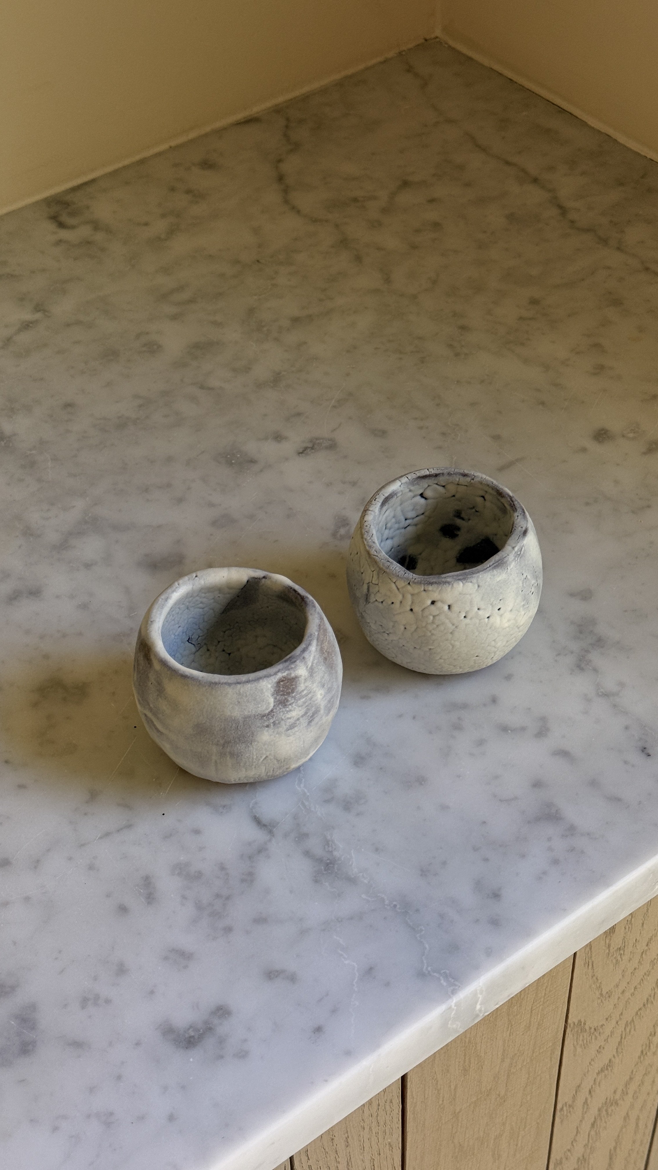 Set of two round handmade ceramic cups in pale blue-grey glaze, one smooth and clouded, the other with a fine white crackle texture