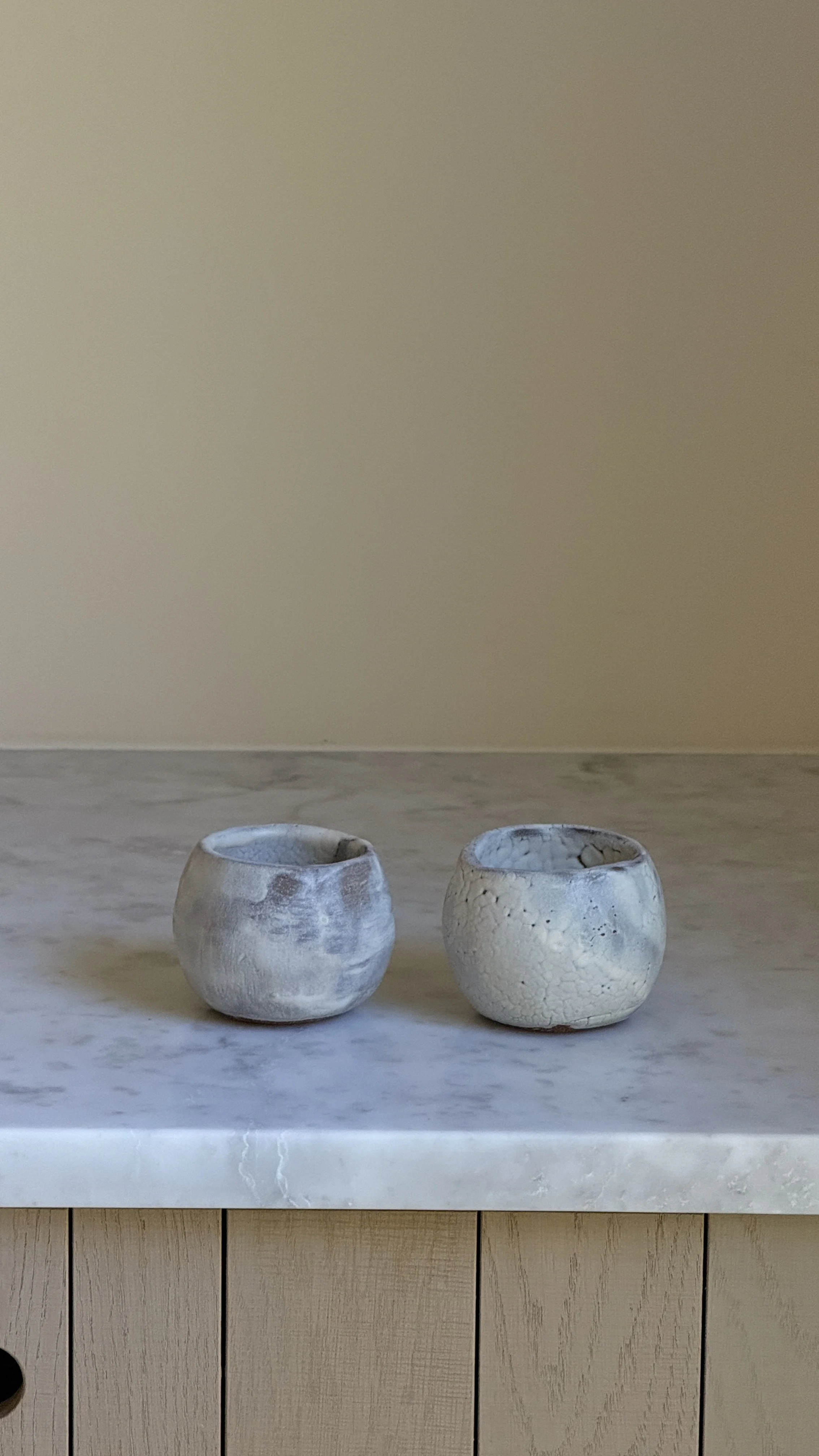 Set of two round handmade ceramic cups in pale blue-grey glaze, one smooth and clouded, the other with a fine white crackle texture