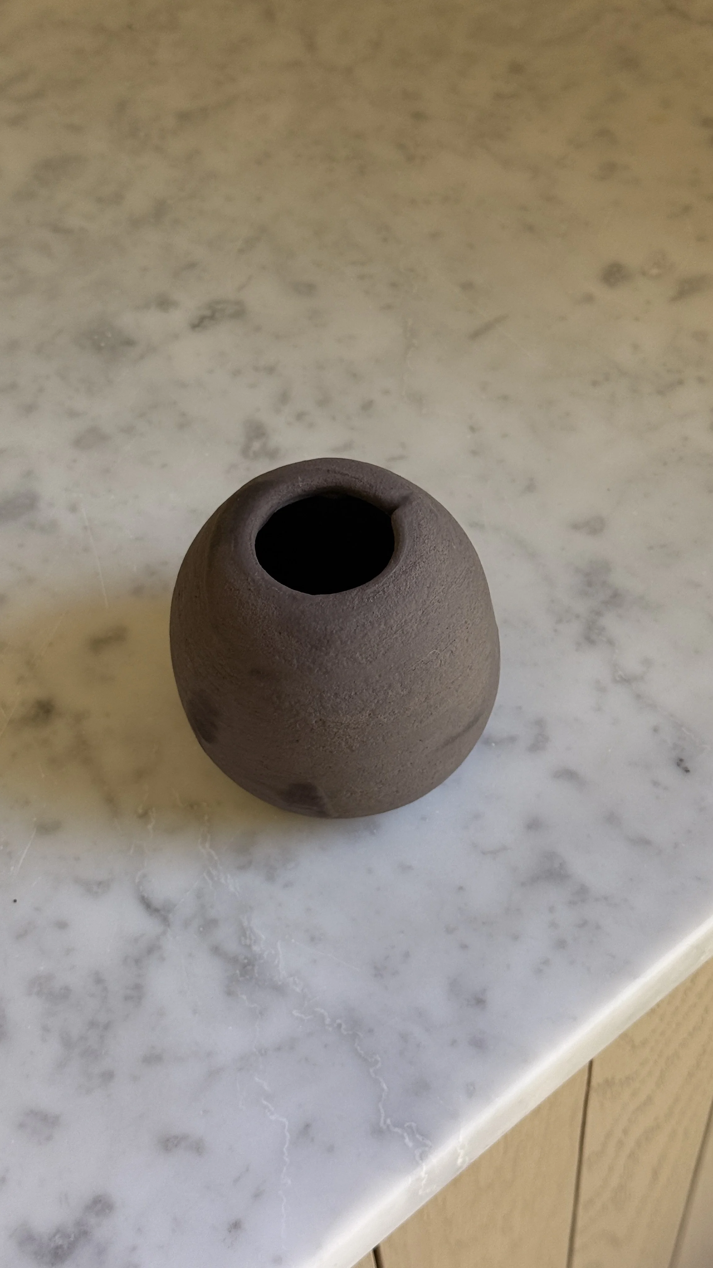 Small round matte brown ceramic bud vase with a narrow opening and a soft hand-pressed dimple on one side