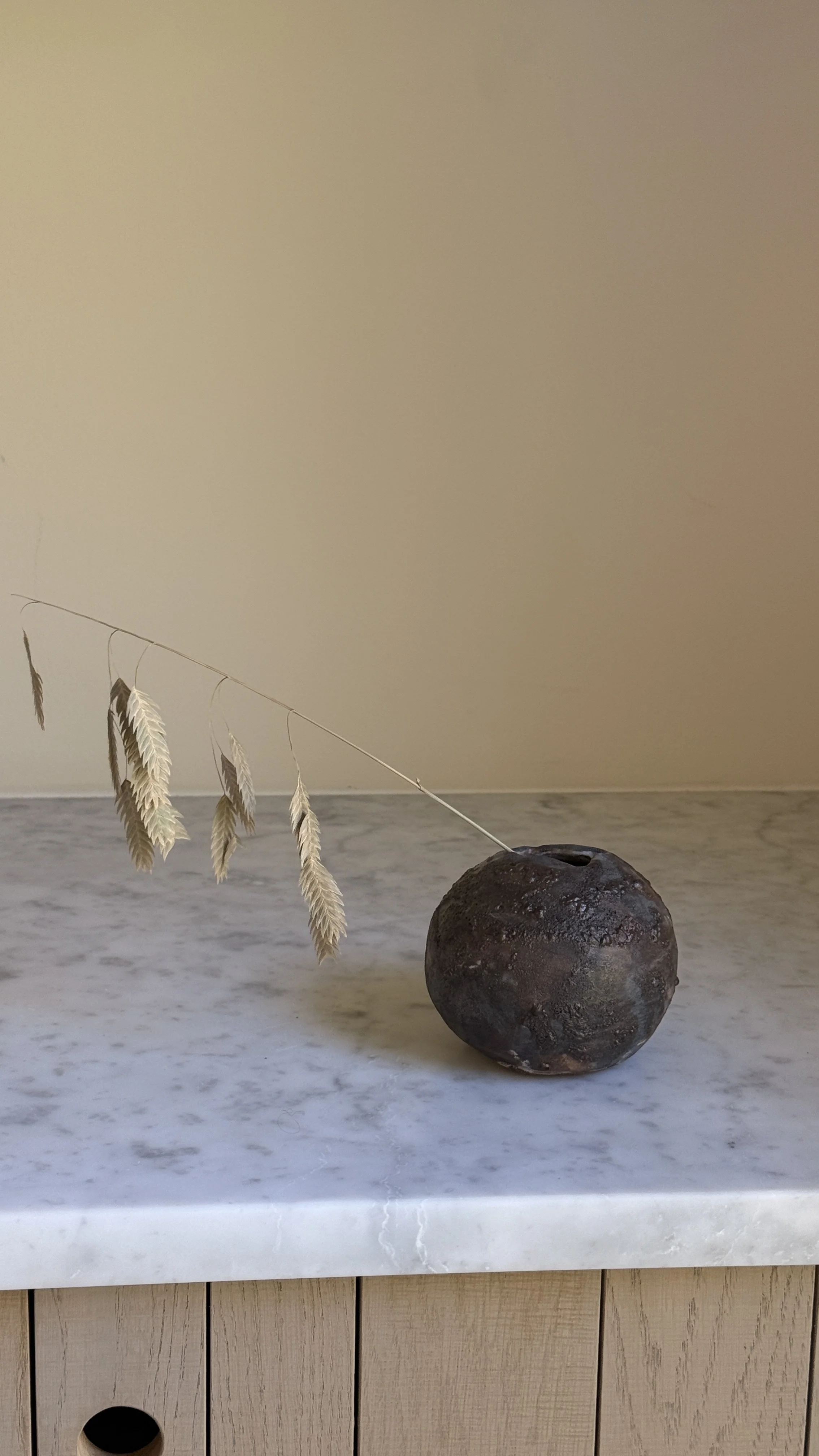 Round dark ceramic moon vase with a textured lava glaze in brown, charcoal, and bronze, and a small opening at the top