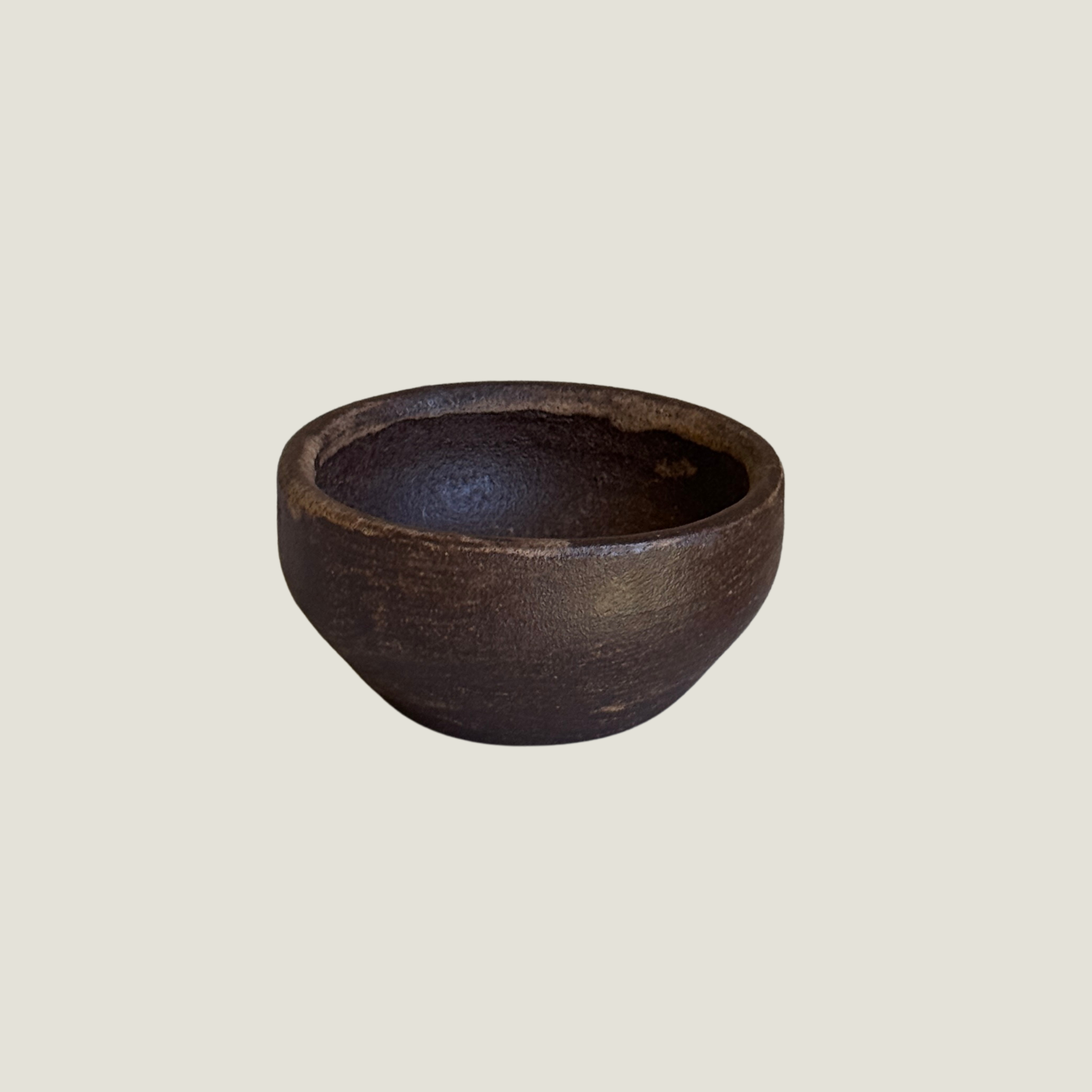 Hearth Bowl – Small Dark Ceramic Bowl.pngSmall dark brown ceramic bowl with a rough matte surface and a lightly worn, lighter rim on a greige background