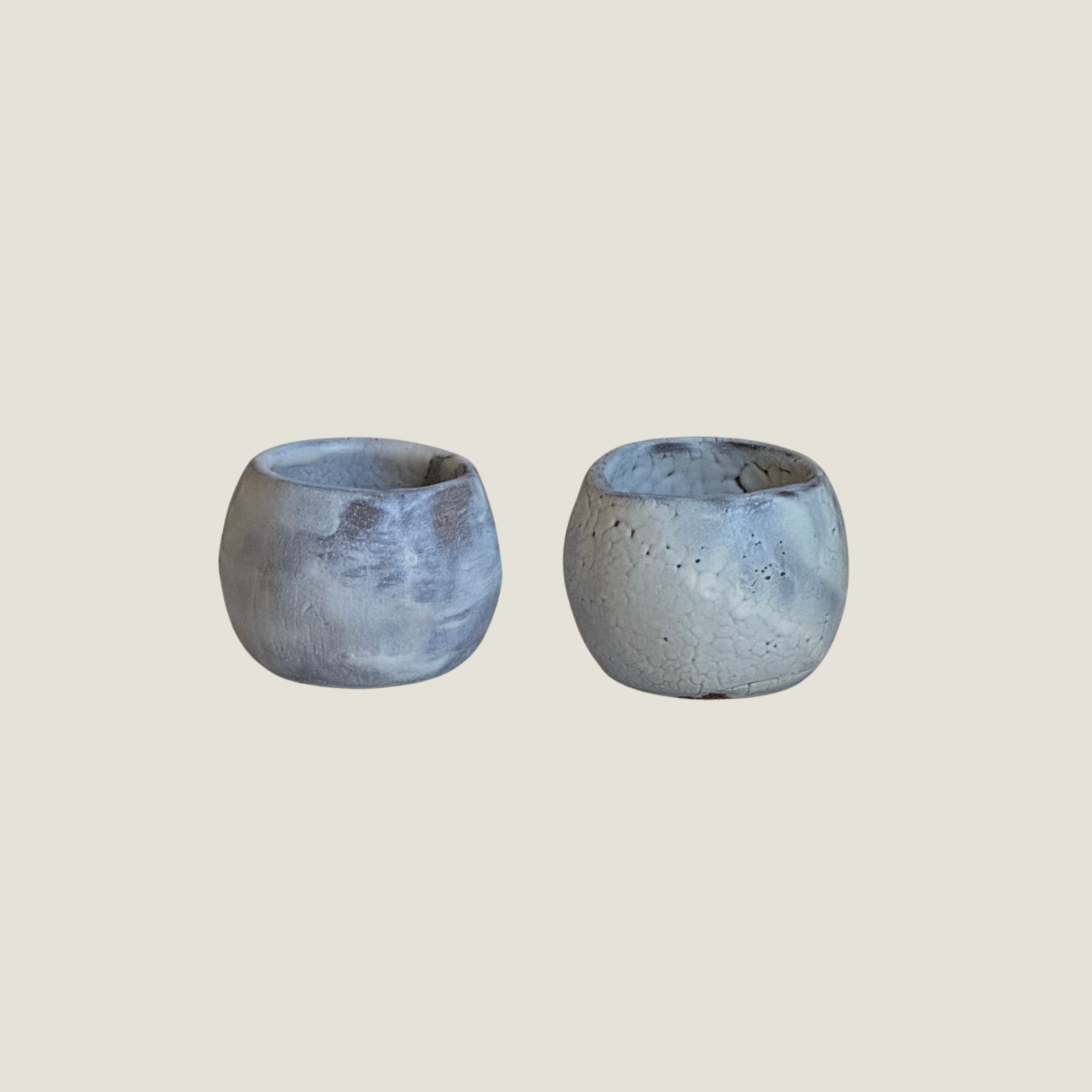 Set of two round handmade ceramic cups in pale blue-grey glaze, one smooth and clouded, the other with a fine white crackle texture