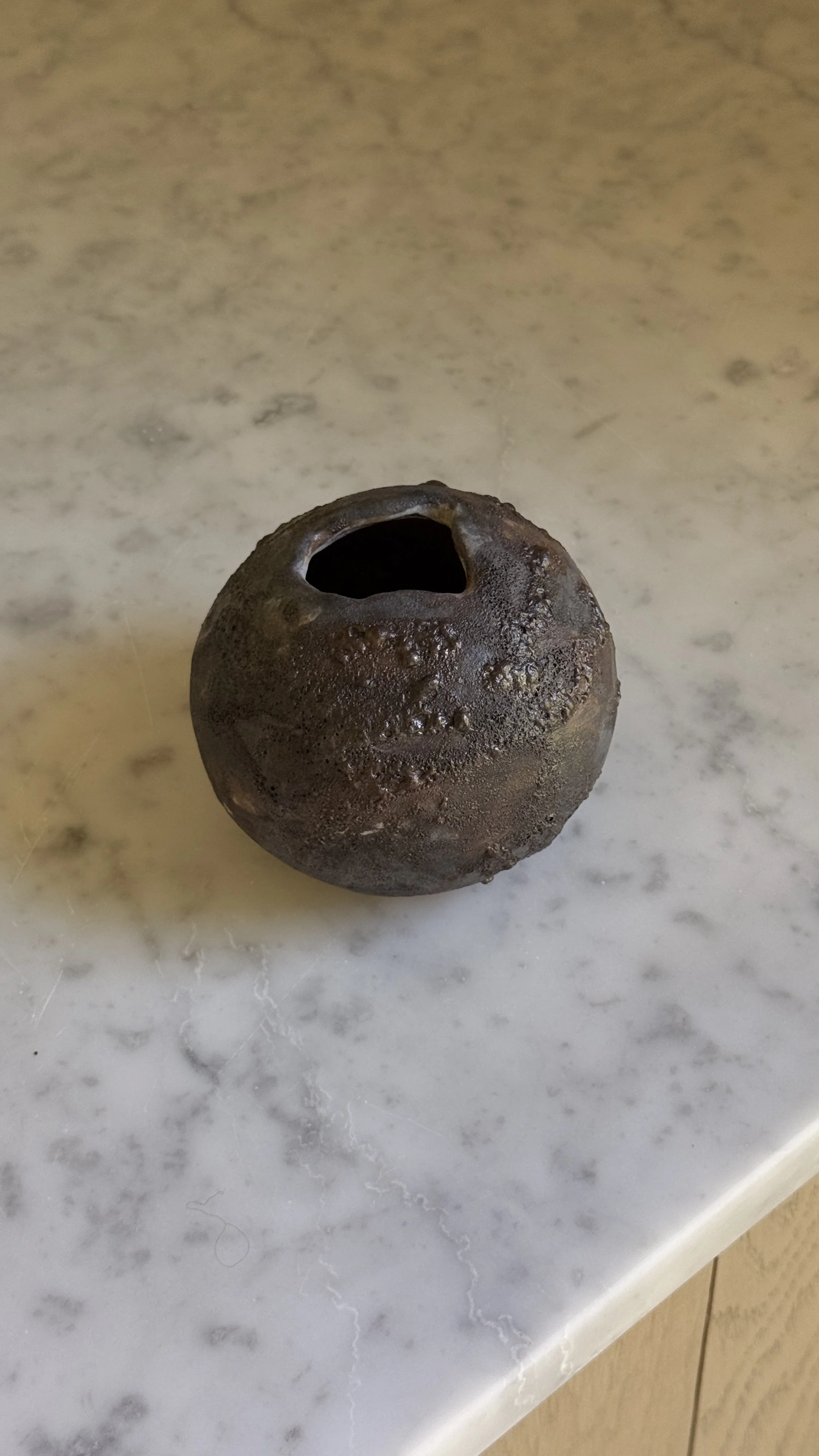 Round dark ceramic moon vase with a textured lava glaze in brown, charcoal, and bronze, and a small opening at the top
