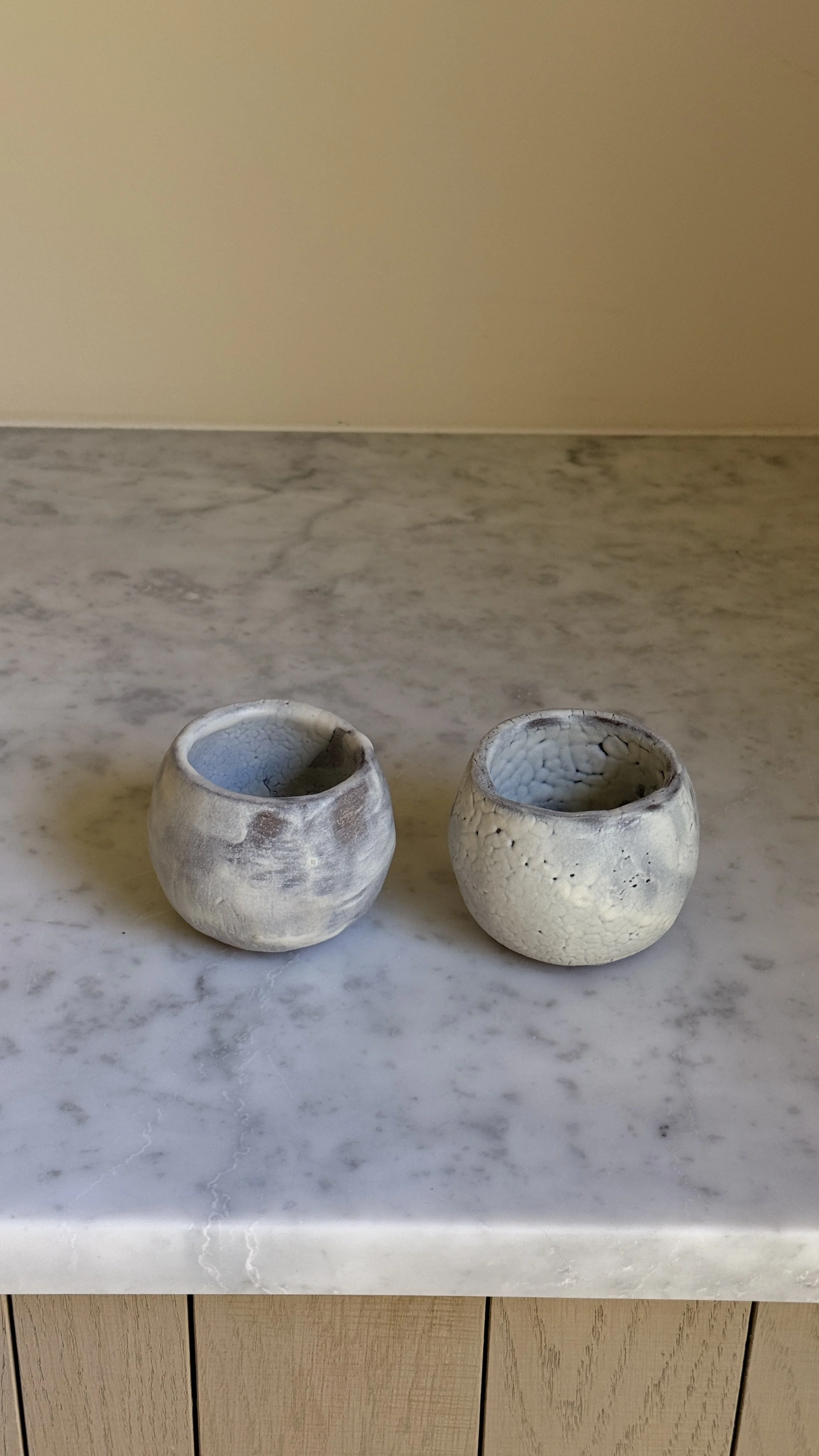 Set of two round handmade ceramic cups in pale blue-grey glaze, one smooth and clouded, the other with a fine white crackle texture
