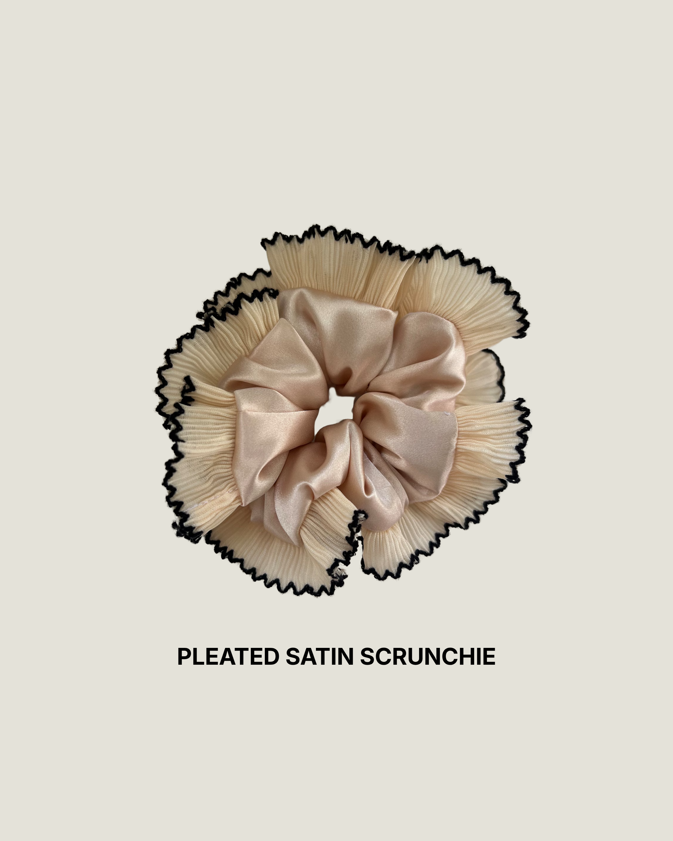 Handmade champagne pleated satin scrunchie with black-edged ruffle on a white background