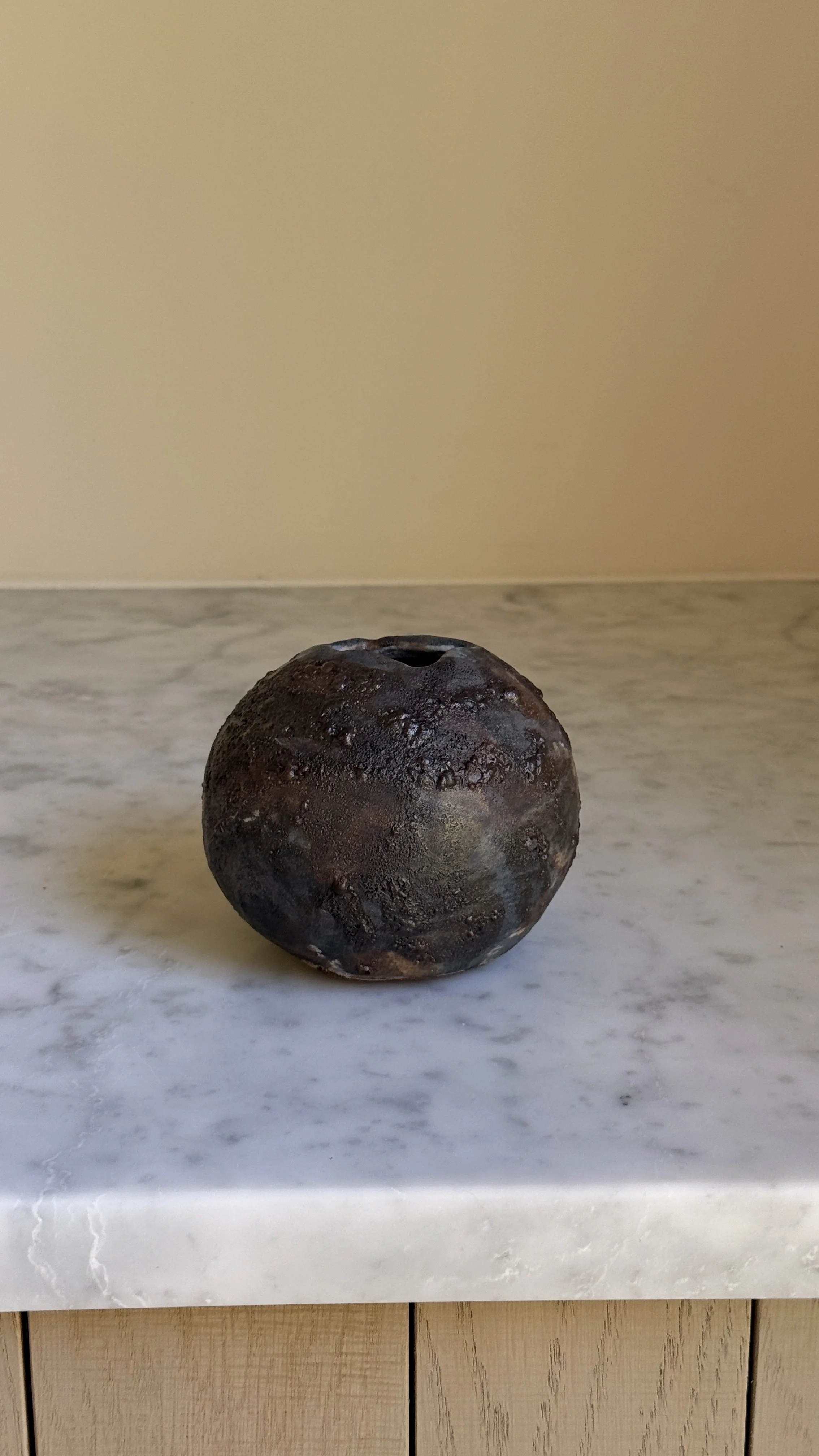 Round dark ceramic moon vase with a textured lava glaze in brown, charcoal, and bronze, and a small opening at the top