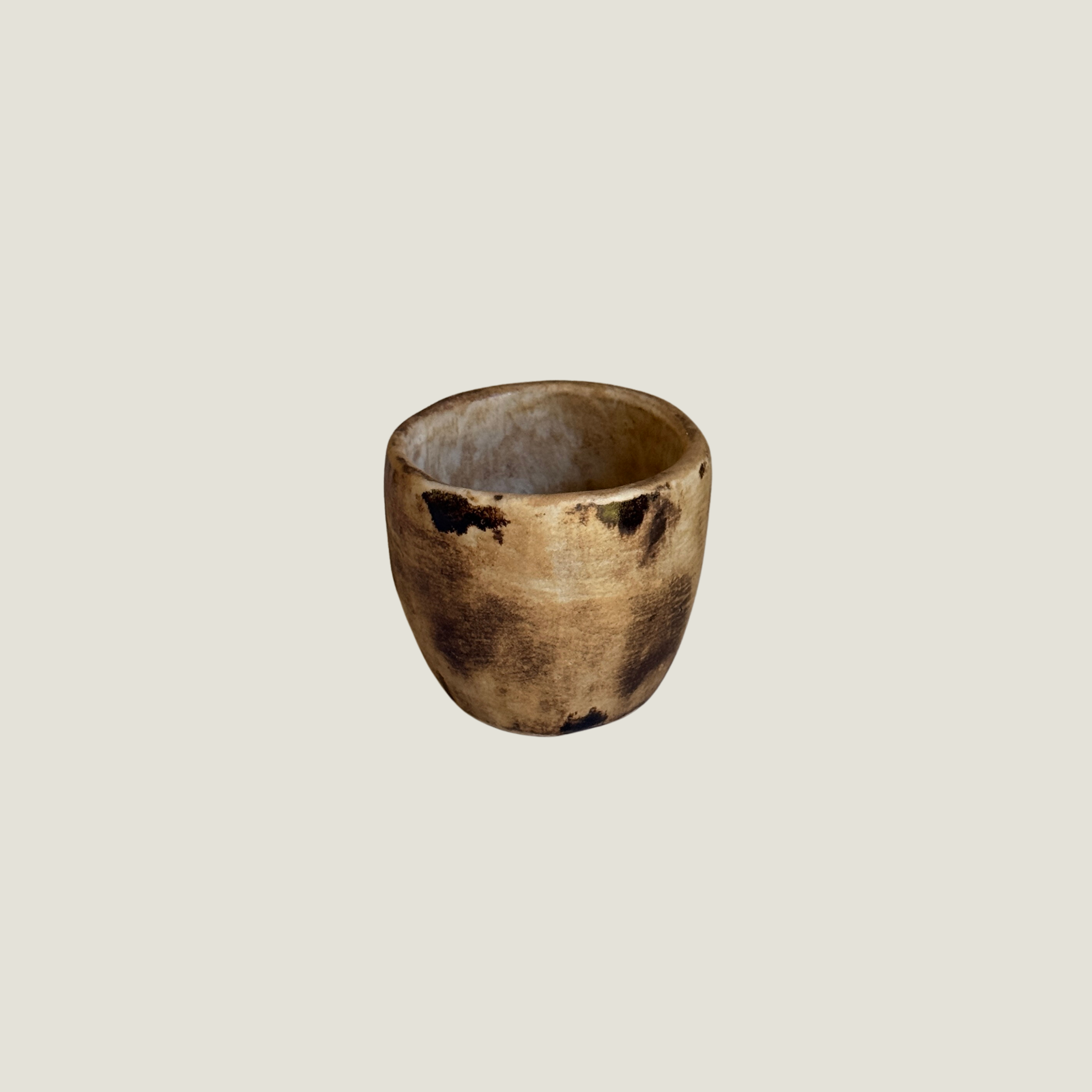 Tapered ceramic cup in warm caramel and sand tones with dark smoky patches on the surface and a pale interior