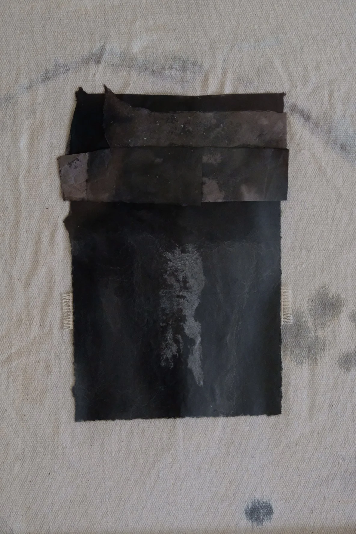 Framed 11 x 14 collage of layered near-black torn paper on pale canvas with grey rings