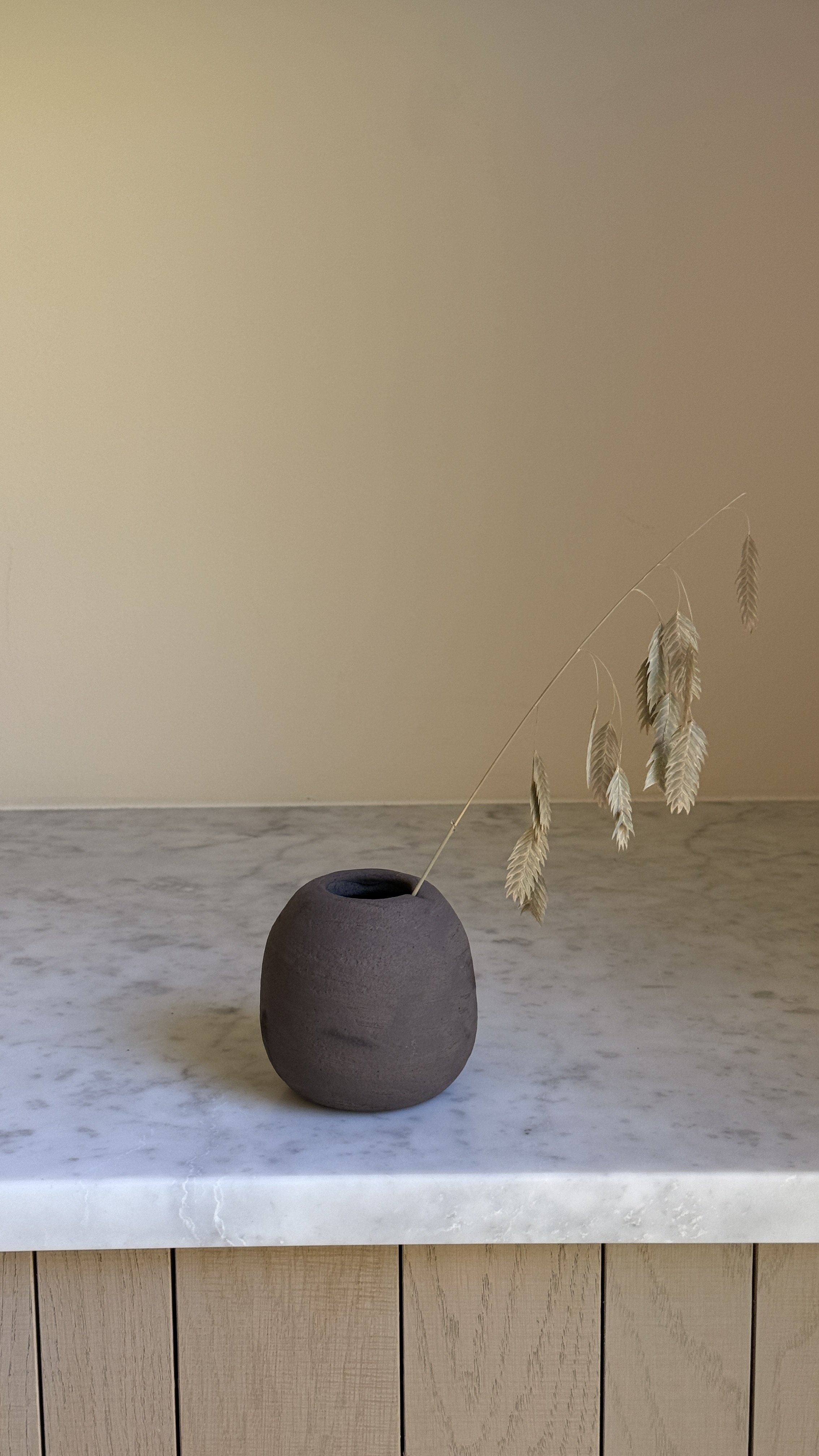 Small round matte brown ceramic bud vase with a narrow opening and a soft hand-pressed dimple on one side