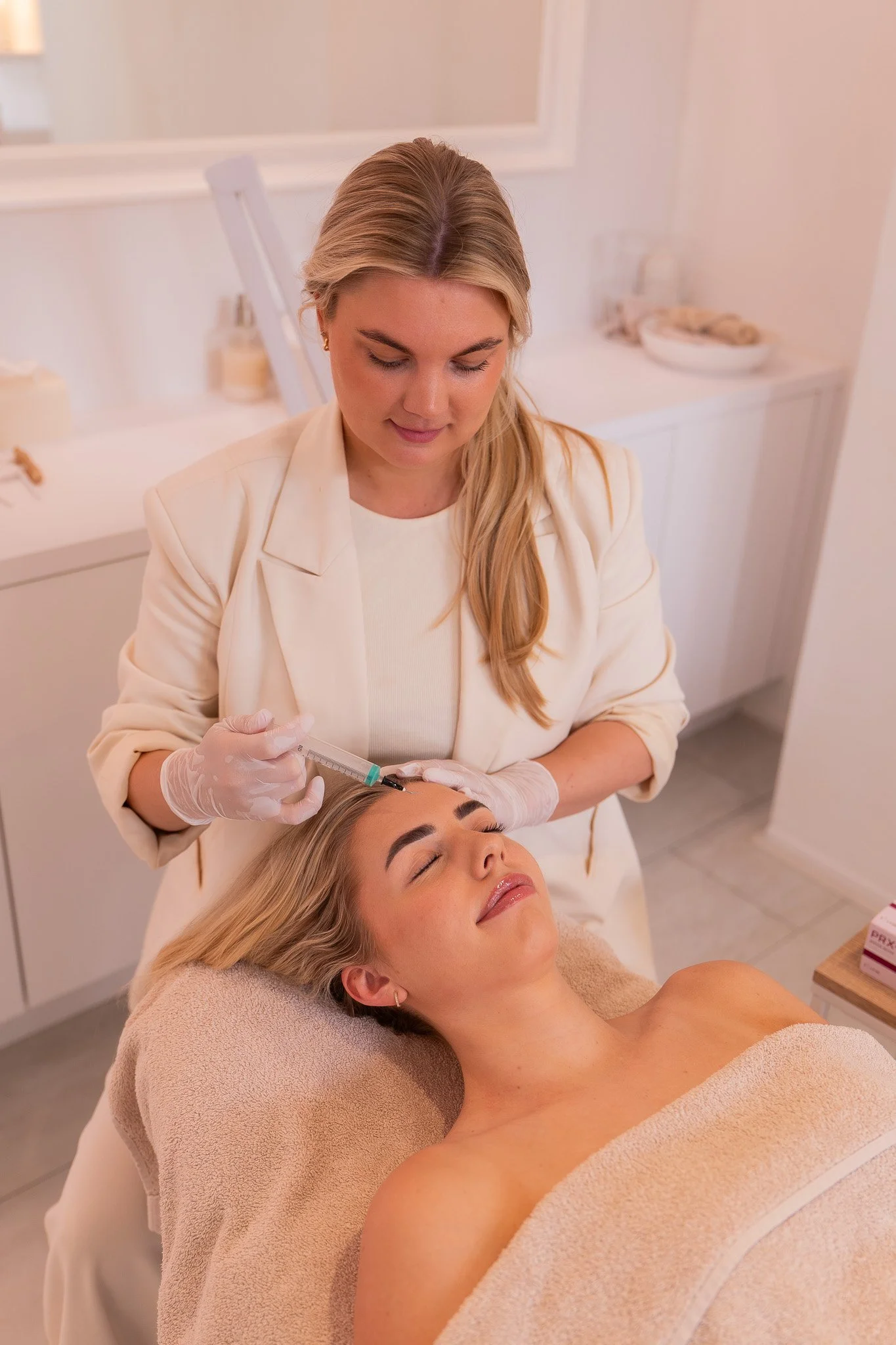 Een vrouw ligt op een behandeltafel en krijgt een gezichtsbehandeling van een schoonheidsspecialist in een schoonheidssalon.