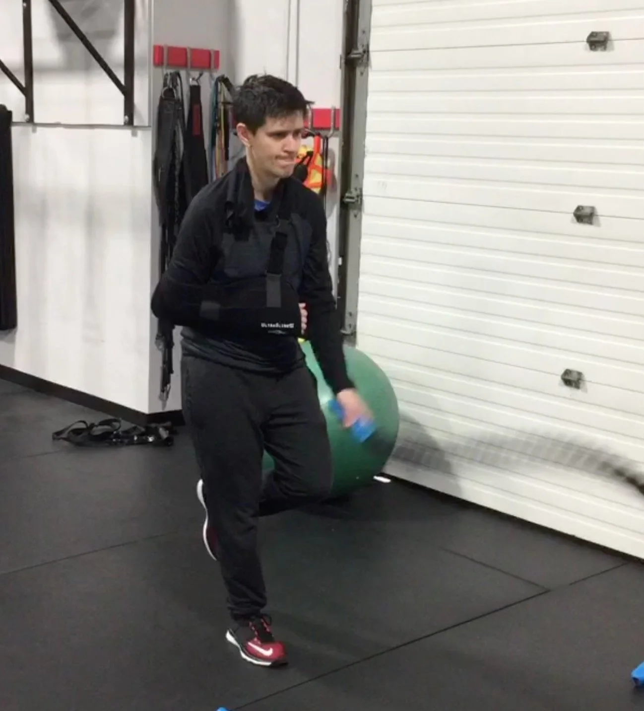 image of a woman dressed in black, wearing a shoulder sling and standing on one leg while exercising