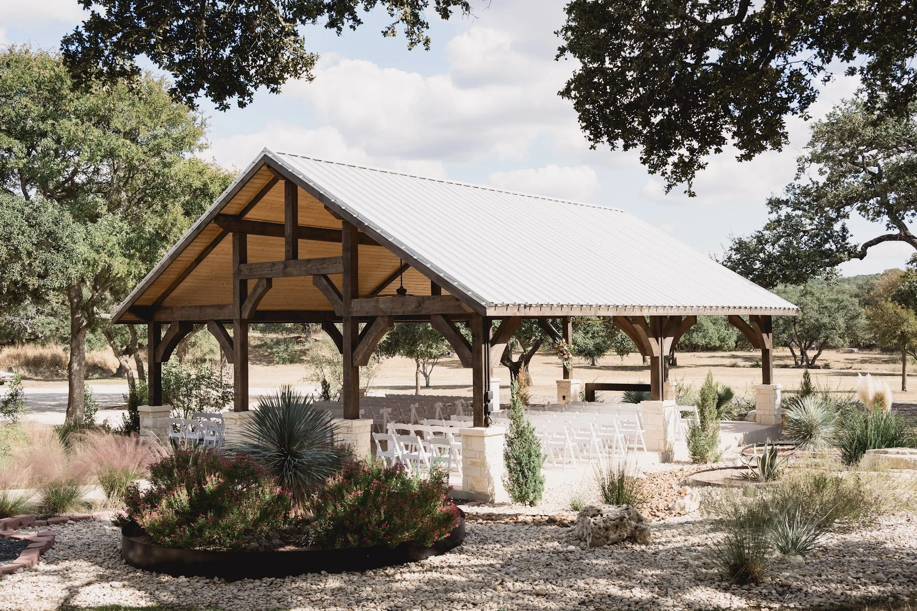 A large backyard with a swing attached to a tree branch, a pavilion with white chairs on one side, and several other trees in the background under a cloudy sky.