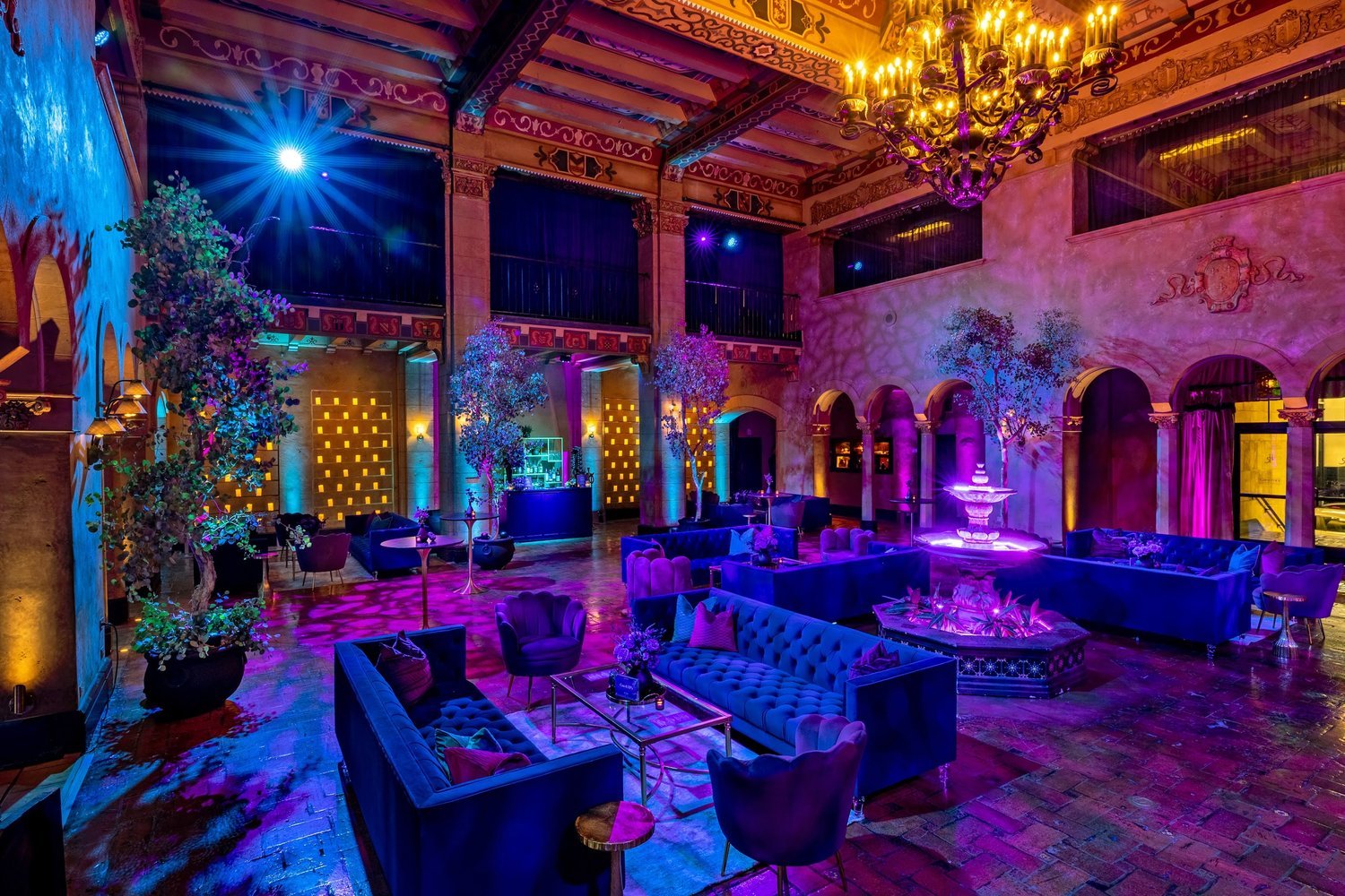 Luxurious hotel lobby with ornate chandelier, colorful lighting, plush seating, and decorative fountain.