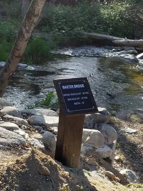 A view of Baxter Bridge at Baxter Ranch, where mountain waters flow beneath a scenic crossing surrounded by forest, rocks, and the natural beauty of the Sierra Nevada foothills.