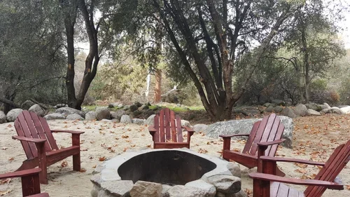 Outdoor fire pit area at Baxter Ranch with Adirondack chairs surrounded by trees and natural rock features, creating a cozy gathering space for guests to relax and enjoy the mountain setting.