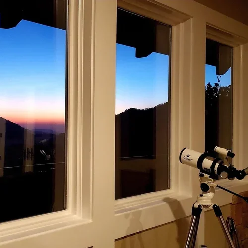 Sunset views from the Hilltop House at Baxter Ranch seen through large windows with a telescope nearby for enjoying mountain scenery and wildlife viewing.