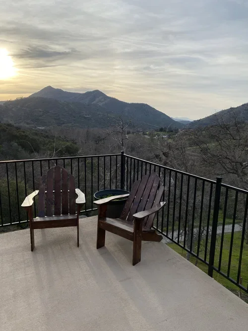 Adirondack chairs on the Hilltop House balcony at Baxter Ranch overlooking a mountain landscape at sunset, offering a peaceful space to relax and enjoy the views.