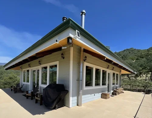 Hilltop House at Baxter Ranch featuring large windows, a spacious outdoor patio, and sweeping mountain views surrounded by the peaceful beauty of the Sierra Nevada landscape.