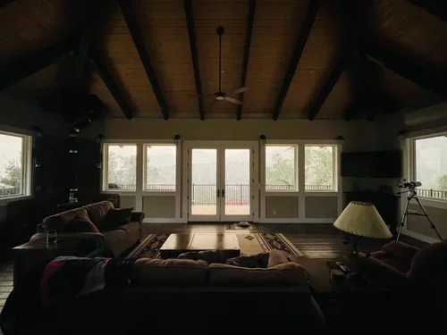 Cozy Hilltop House living room at Baxter Ranch featuring vaulted wood ceilings, large windows, comfortable seating, and a telescope overlooking the peaceful mountain landscape on a foggy morning.