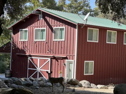 The red barn at Baxter Ranch surrounded by forest, natural rock features, and mountain wildlife, showcasing the rustic charm of this unique mountain retreat.