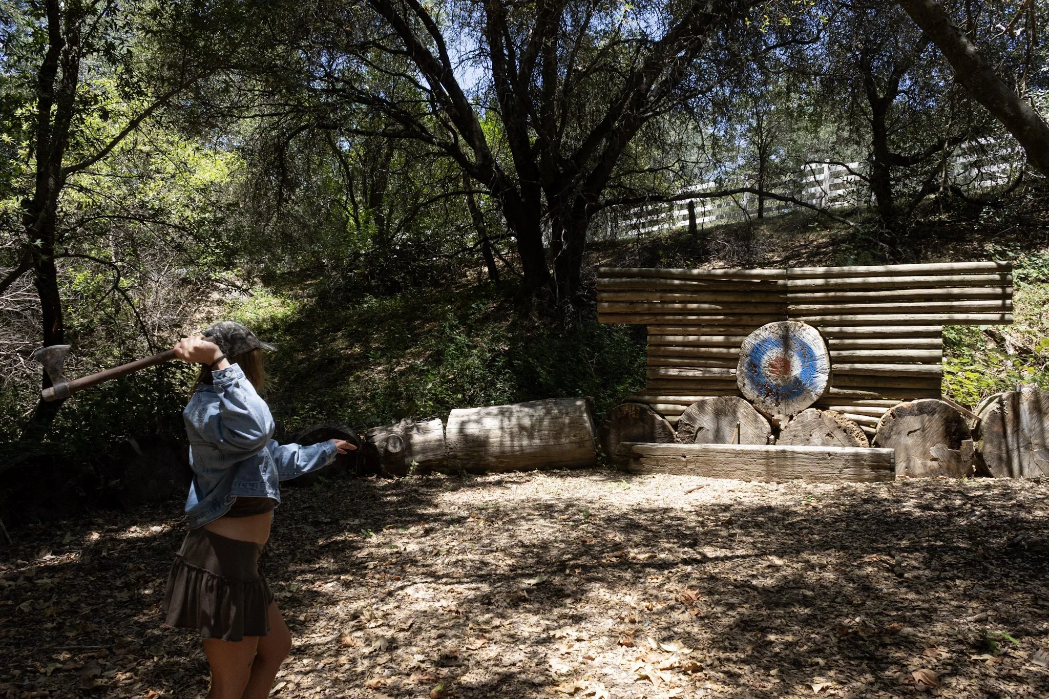 Axe throwing activity at Baxter Ranch in a wooded outdoor setting, featuring a wooden target, log pile, and natural mountain surroundings for guests to enjoy.