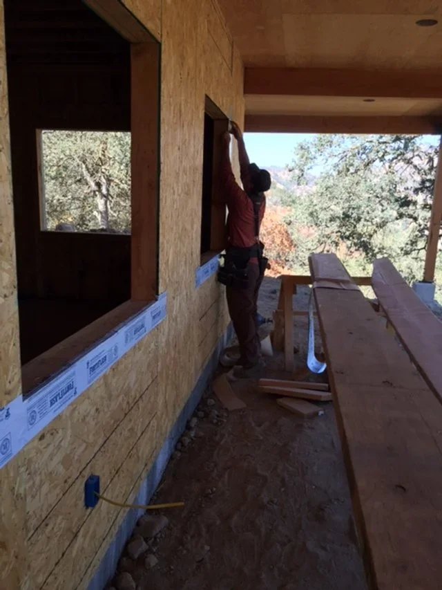 The construction of Hilltop House at Baxter Ranch, capturing the craftsmanship and careful building process as windows and exterior details take shape among the trees.