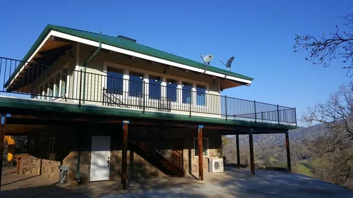 Hilltop House at Baxter Ranch featuring an elevated design, spacious balcony, and scenic views of surrounding trees and mountain hills under a clear blue sky.