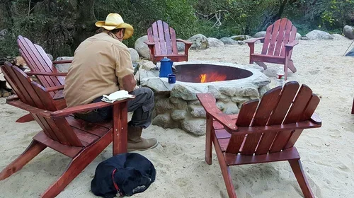 Guests relaxing around the fire pit at Baxter Ranch, with comfortable outdoor seating, forest surroundings, and Gunner the ranch dog enjoying the peaceful mountain setting.