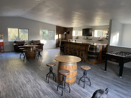 Entertainment Barn lounge at Baxter Ranch featuring rustic barrel furnishings, a custom bar area, foosball table, and comfortable seating designed for group gatherings and mountain retreats.