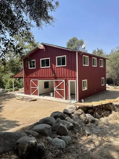 Entertainment Barn at Baxter Ranch, a two-story red barn-style retreat surrounded by trees, natural rock features, and the peaceful landscape of this mountain property.