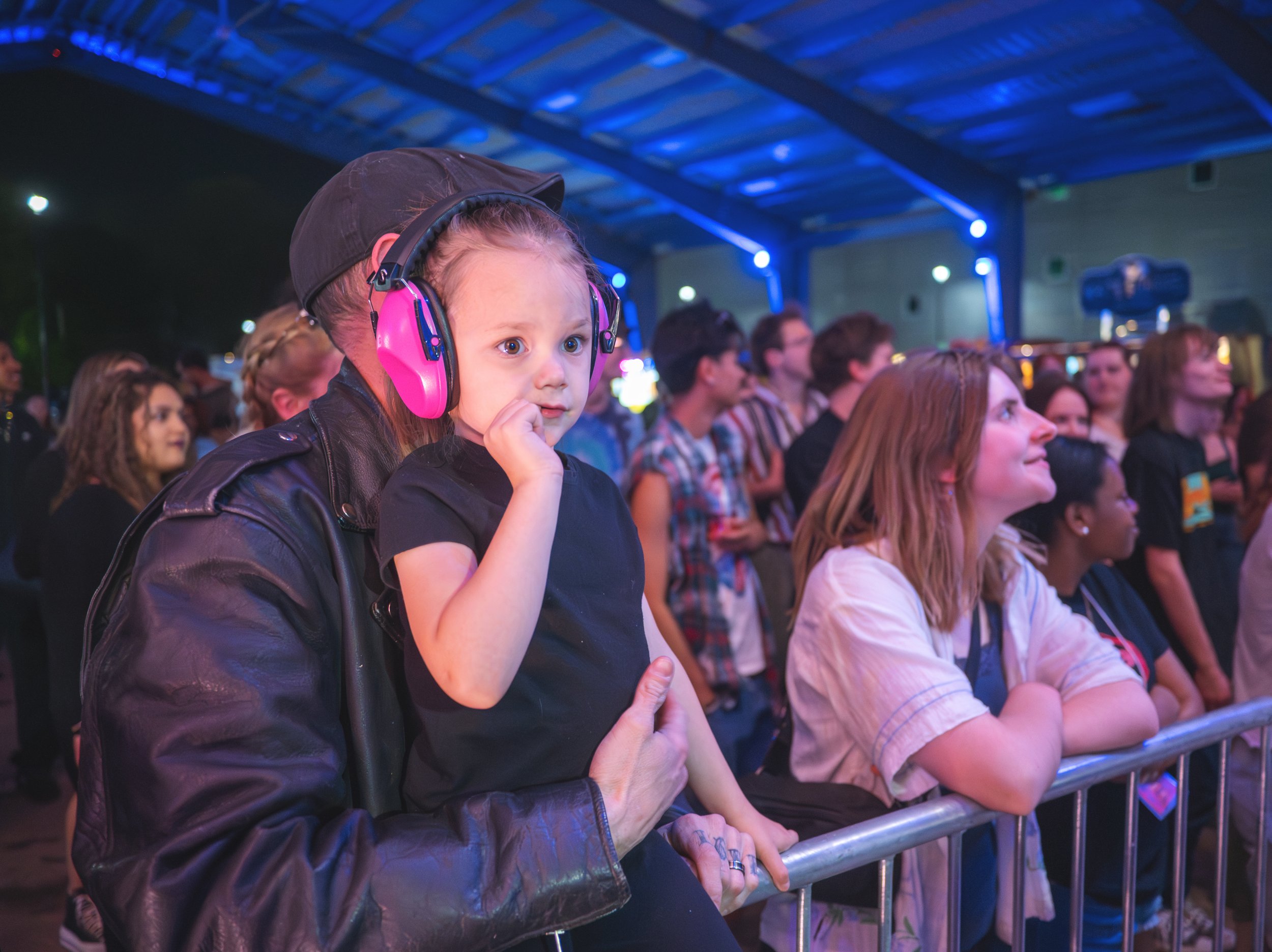 A crowd of people at night watching Girl Tones at Mayhem 2026, with a young girl wearing pink noise-canceling headphones in the foreground.