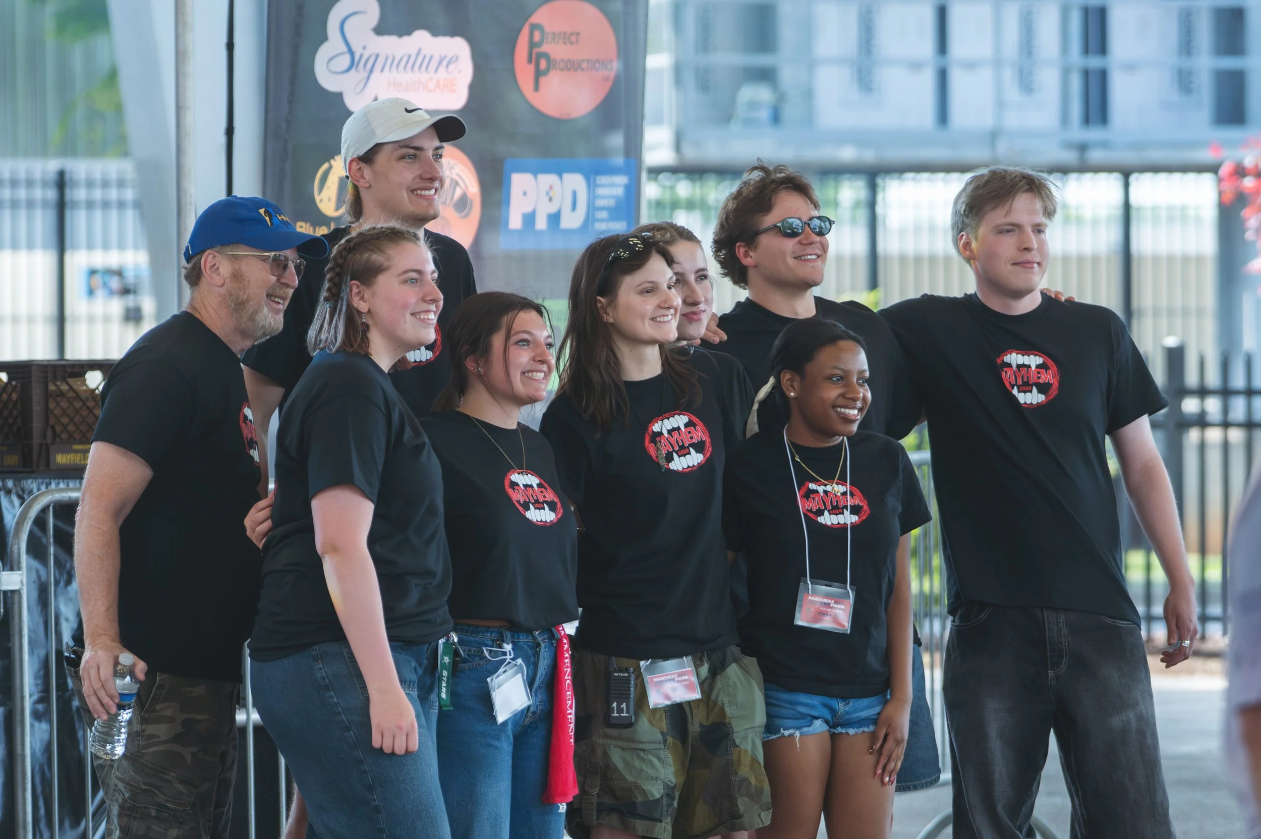 A group of the WWHR Revolution 91.7 staff posing for a photo at the 2026 Mayhem relaunch, with logos in the background including Signature Healthcare and Perfect Productions.