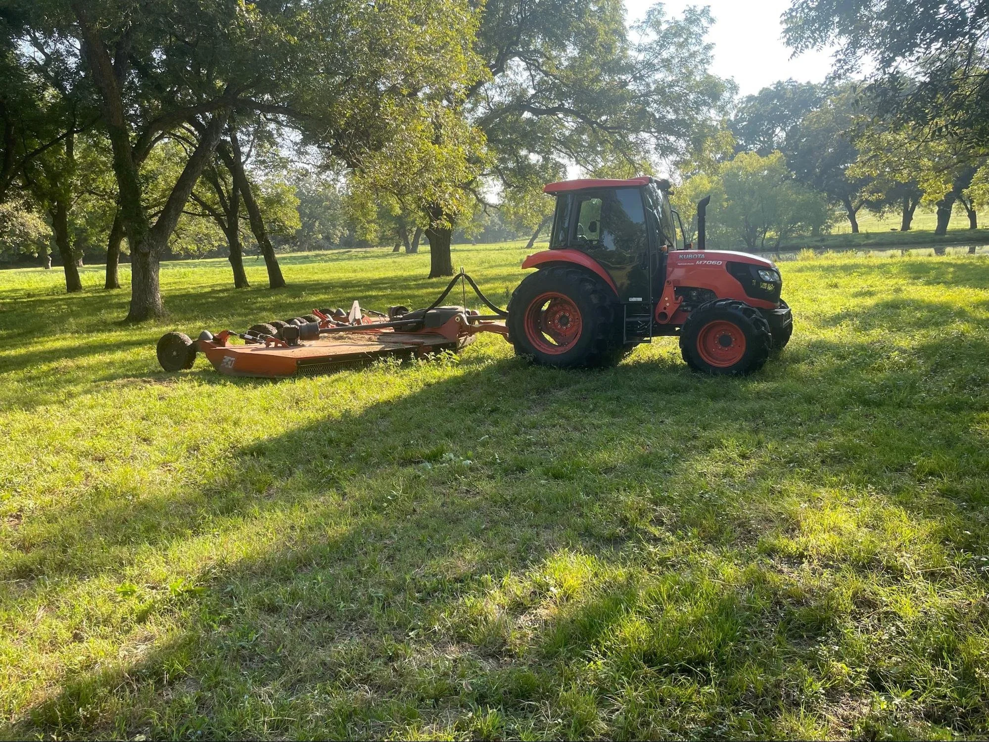 Tractor mower on green field of grass surrounded by trees in Garland, TX.