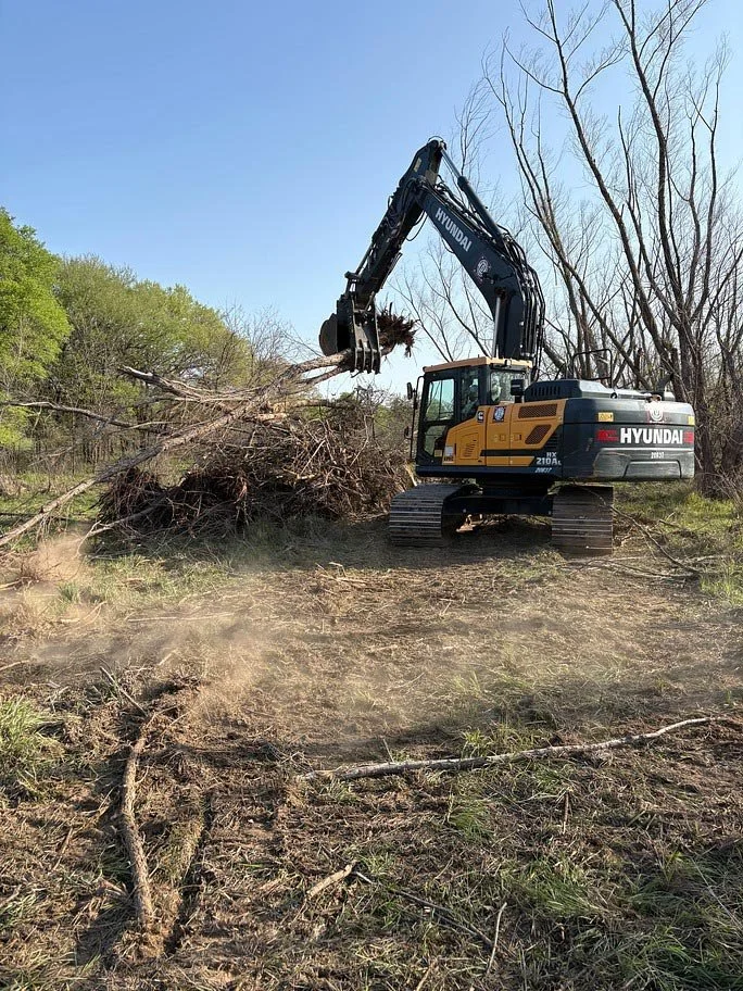Land clearing machinery uses a grapple bucket to move large limbs
