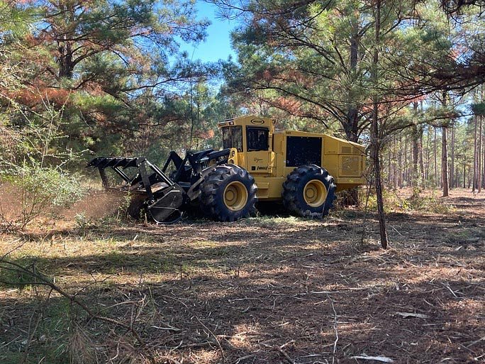 Yellow land-clearing equipment processing brush in a wooded area